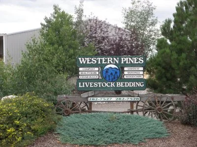 Sign for Western Pines Livestock Bedding surrounded by trees and bushes in a landscaped area.