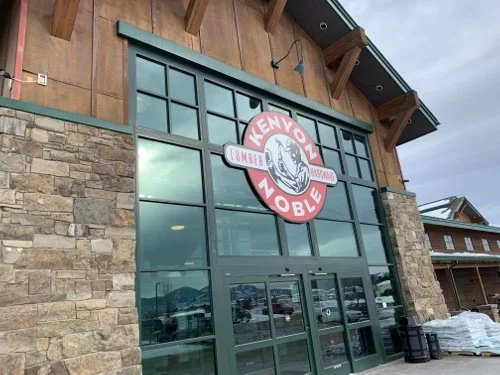 Exterior of a building with large glass windows and a stone facade, featuring a sign for Kenyo Noble and a cat logo.
