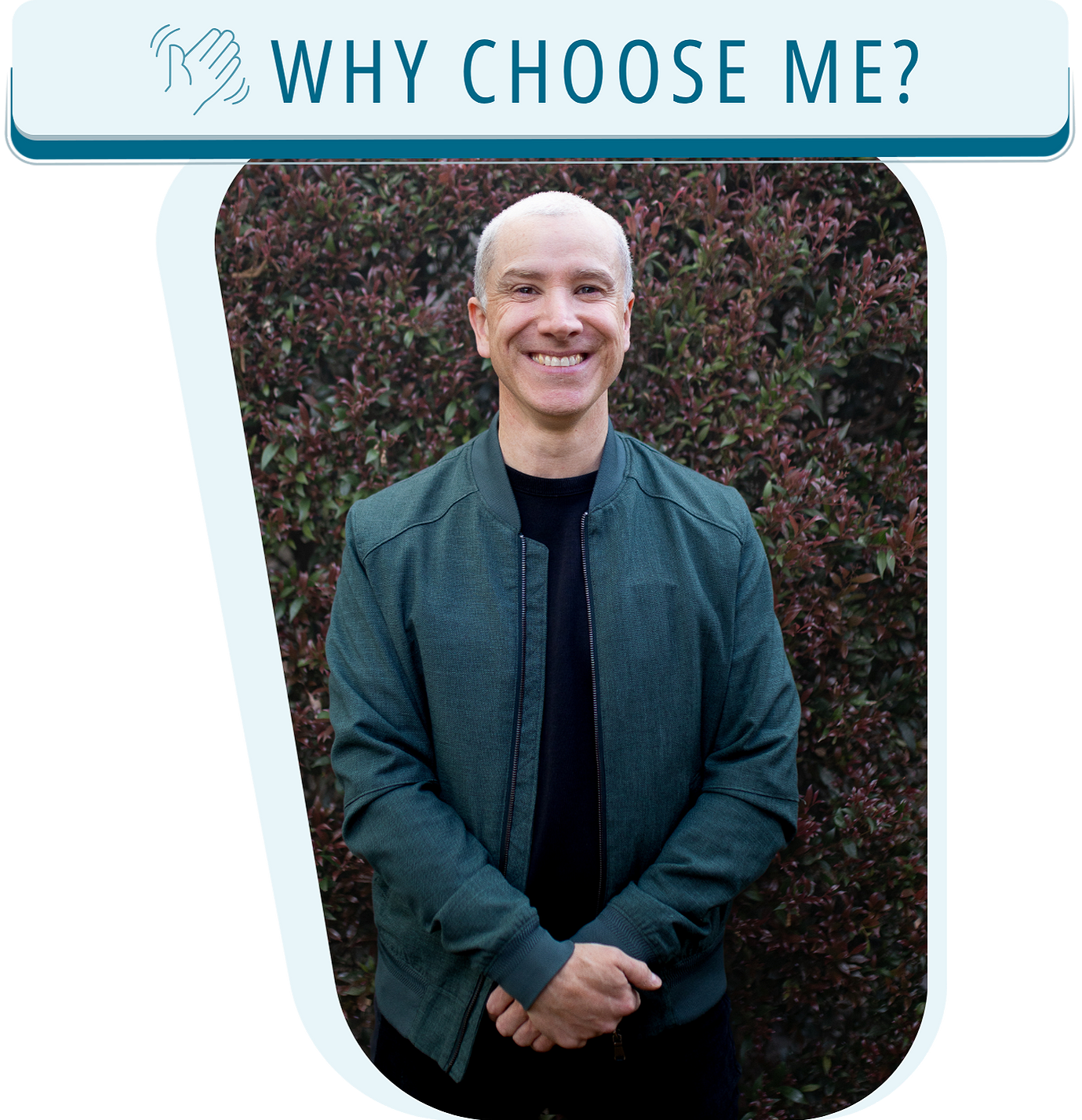 A smiling man standing outdoors in front of a dense bush with dark red leaves, wearing a dark green jacket over a black shirt.