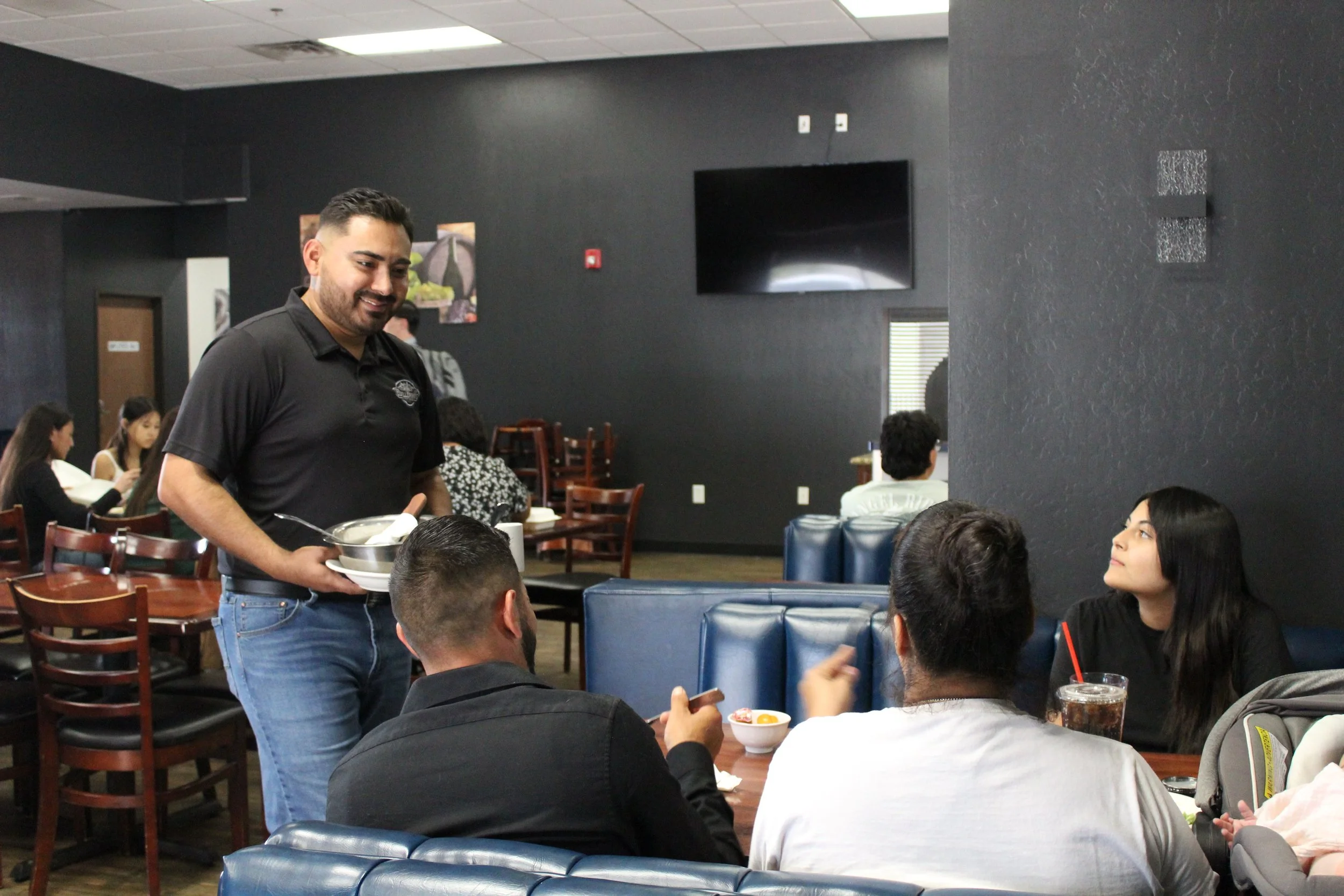 A waiter taking orders from customers in a restaurant, with people seated at tables.