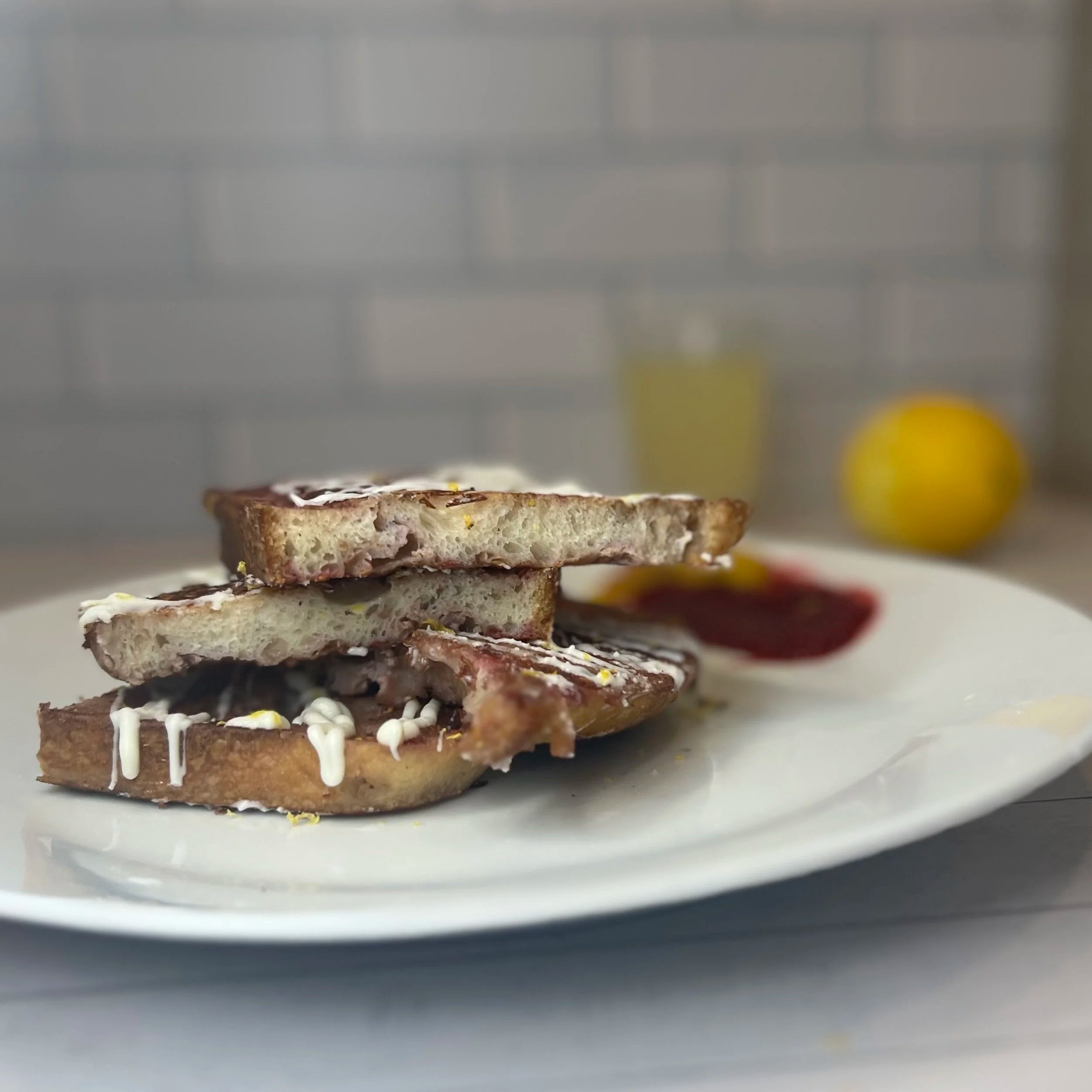 A plate with grilled cheese sandwiches, some lemon slices, and a beverage in the background.