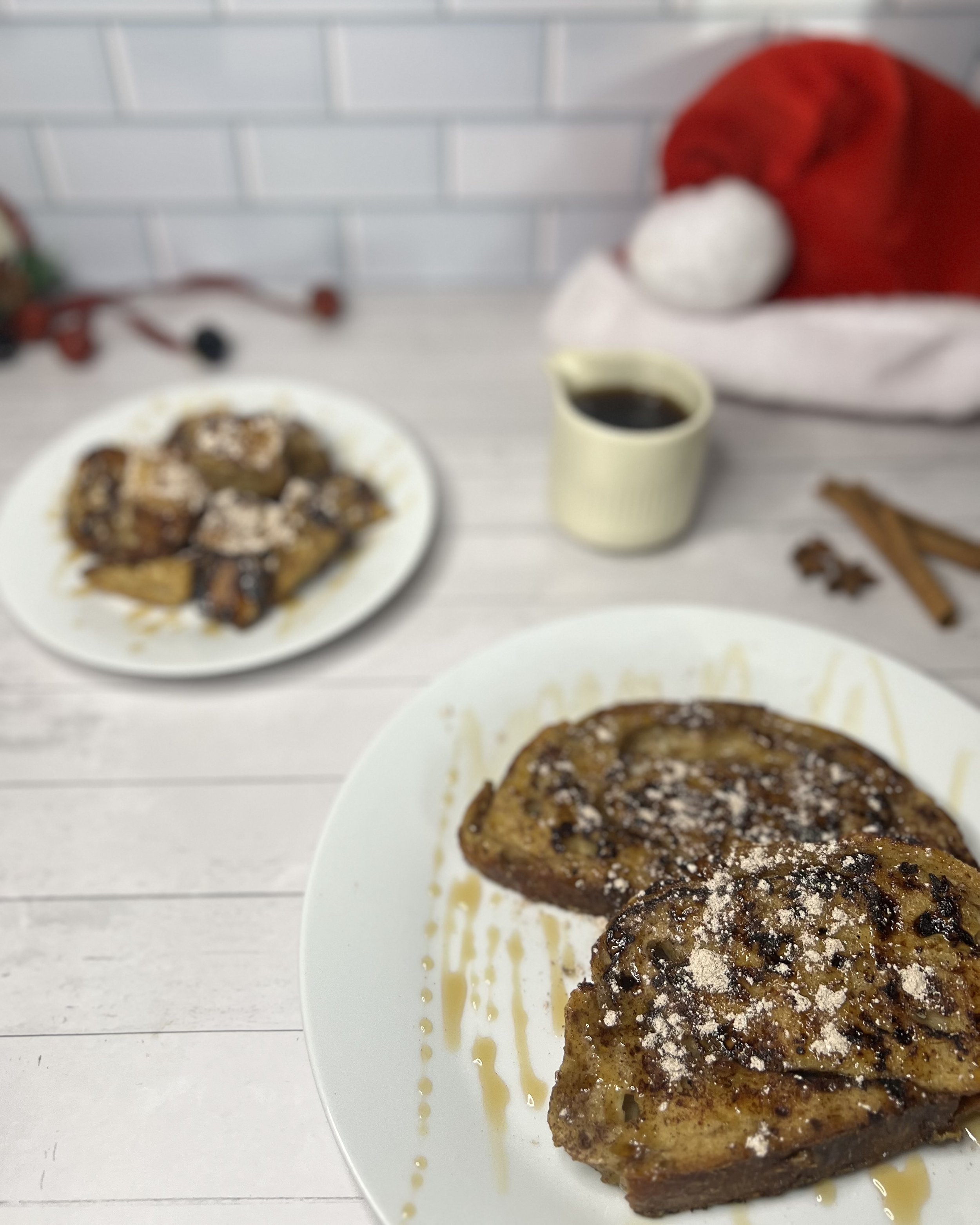 French toast with syrup and powdered sugar on a white plate, with a cup of coffee in the background, and a Christmas Santa hat in a festive setting.