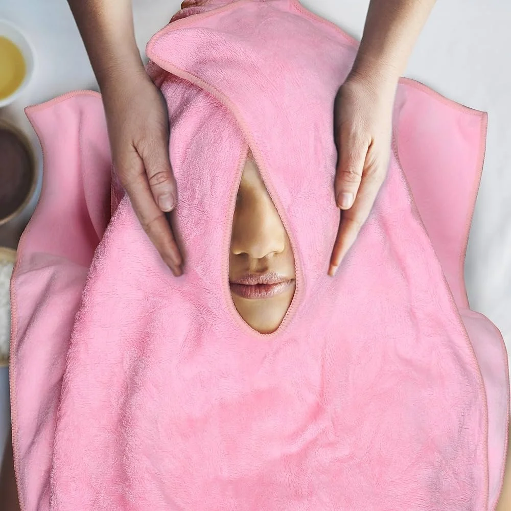 Person receiving a facial massage with a pink towel covering their face and a small opening revealing part of their lips and nose.