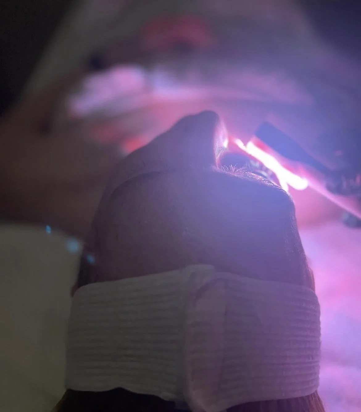 Person holding a smartphone, taking a selfie in a mirror with purple and pink lighting.