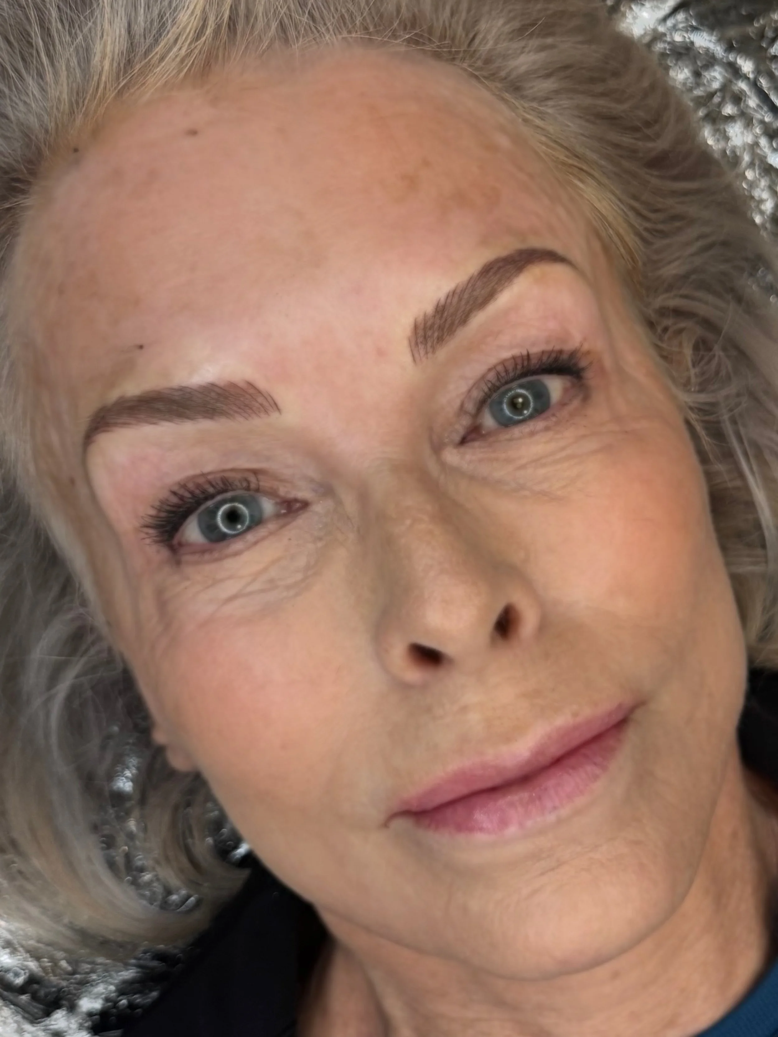 Close-up of a woman with blonde hair and blue eyes, lying down on a surface with a sparkle background, smiling softly.