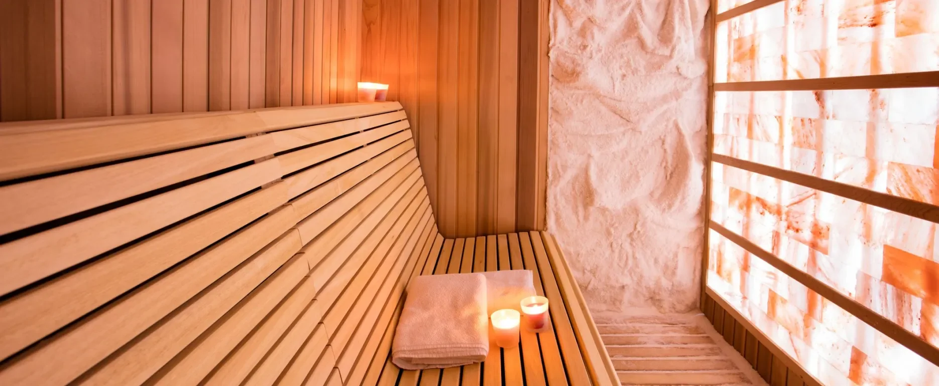 Sauna room with wooden benches, candles, folded towel, and salt wall.