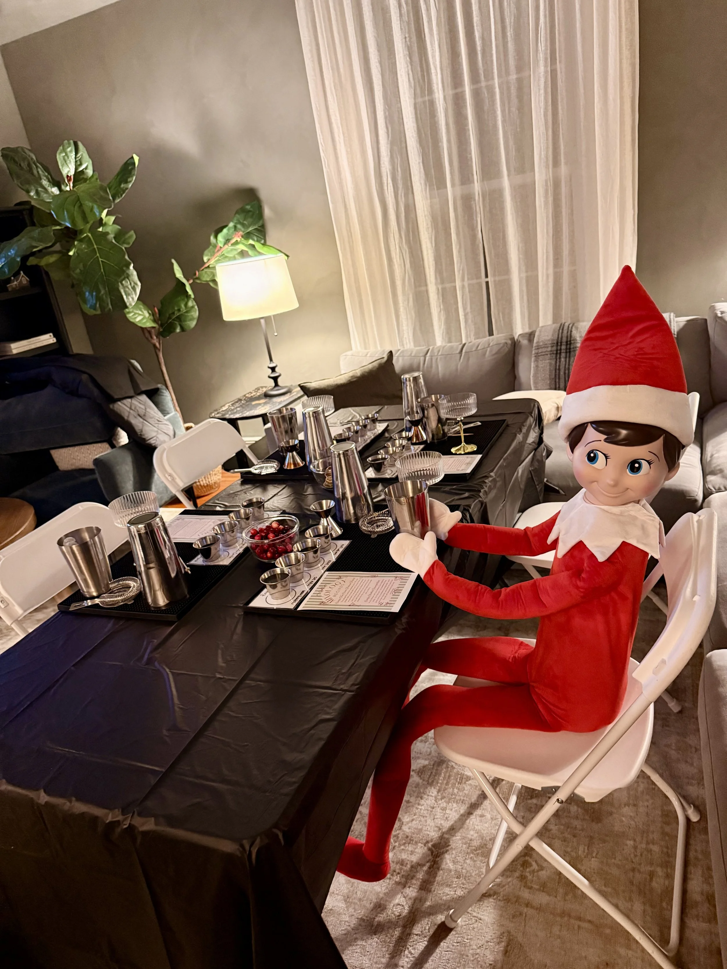 A person dressed as an elf sitting at a dining table decorated for Christmas with a Santa hat, table setting, and a small bowl of cranberries.