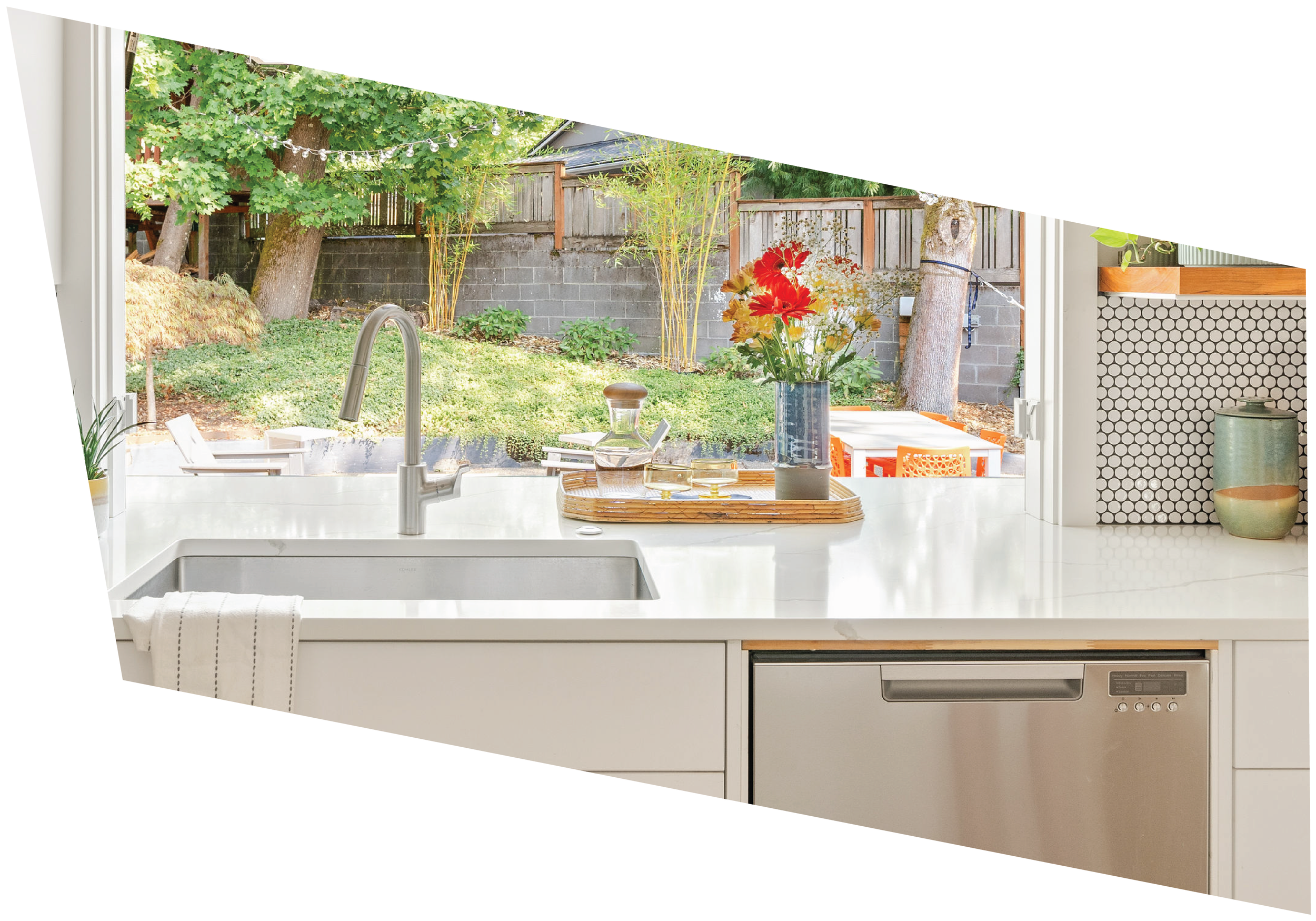 Kitchen with white marble countertop, vase of red and white flowers, view of backyard with trees, wooden fence, and string lights