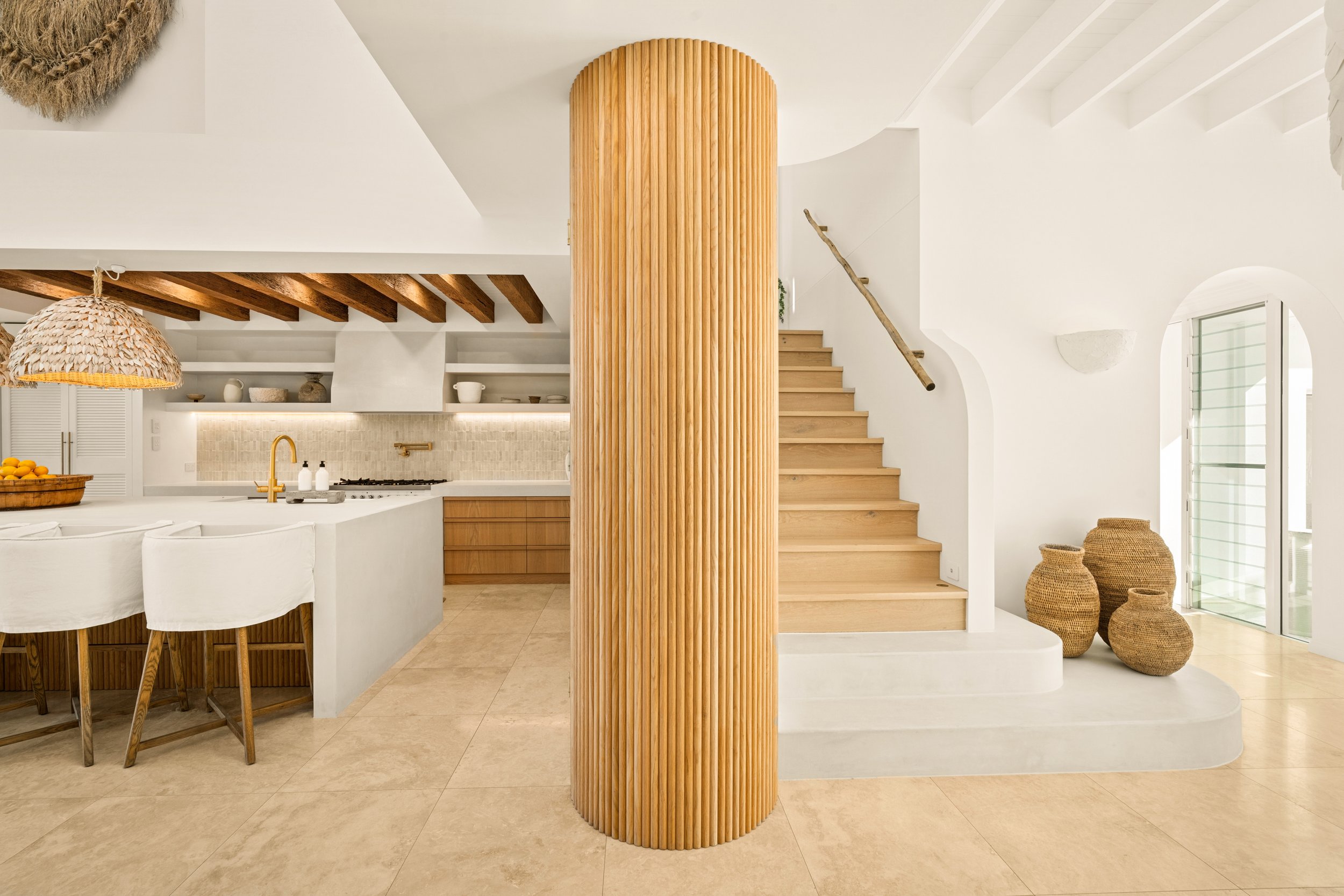 Interior of a modern, minimalist kitchen and staircase with white walls, wooden accents, and woven baskets.