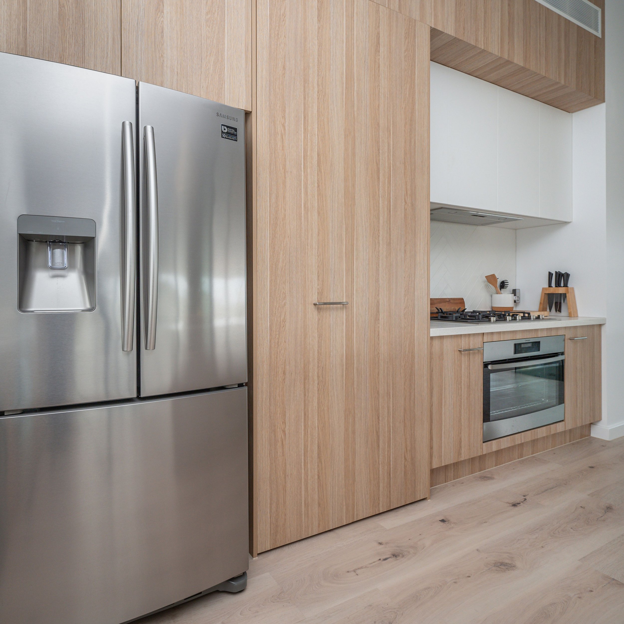 A modern kitchen with a stainless steel refrigerator and wooden cabinets, a stove, and minimal decor.