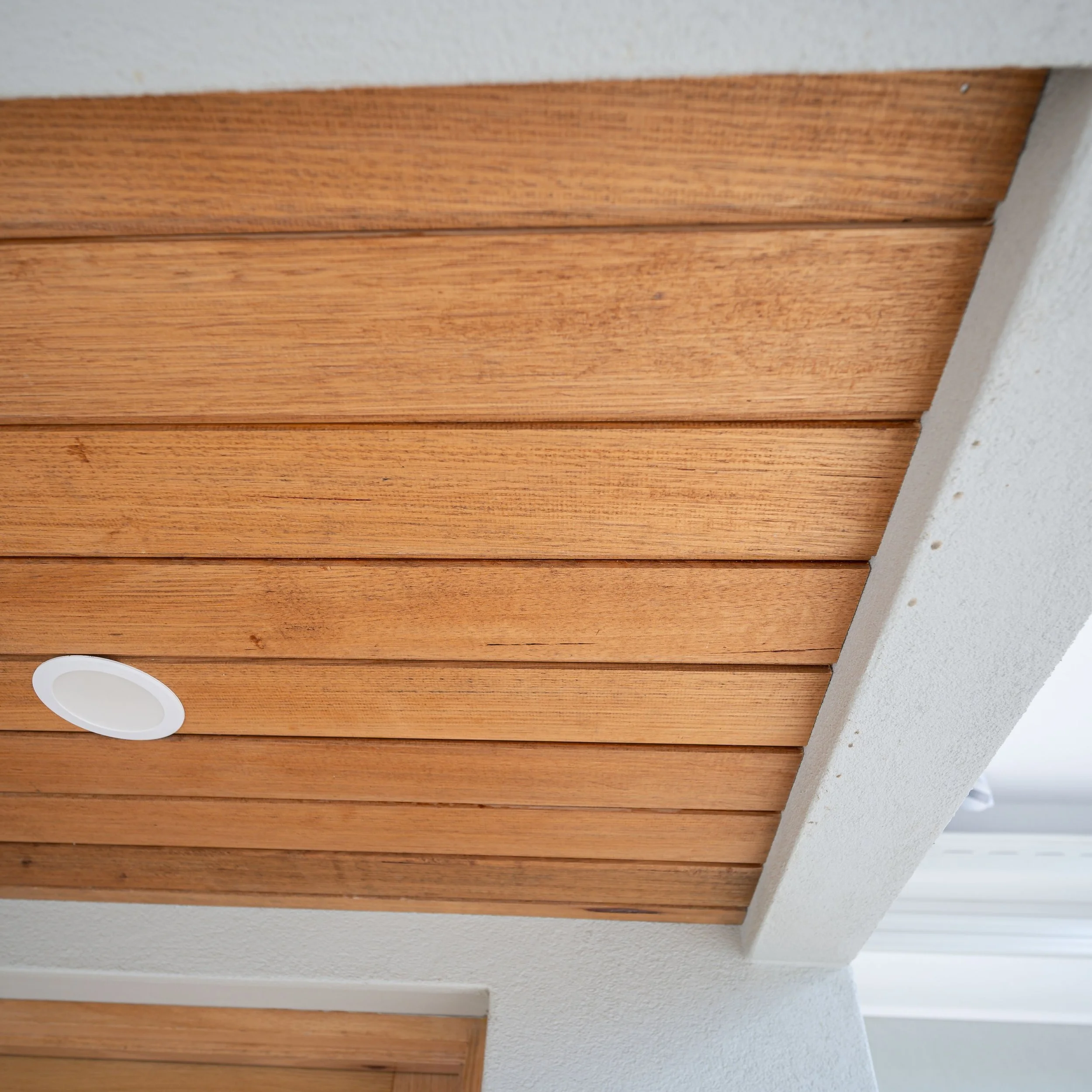 Ceiling with wooden planks, white recessed lighting, and a white textured surface.