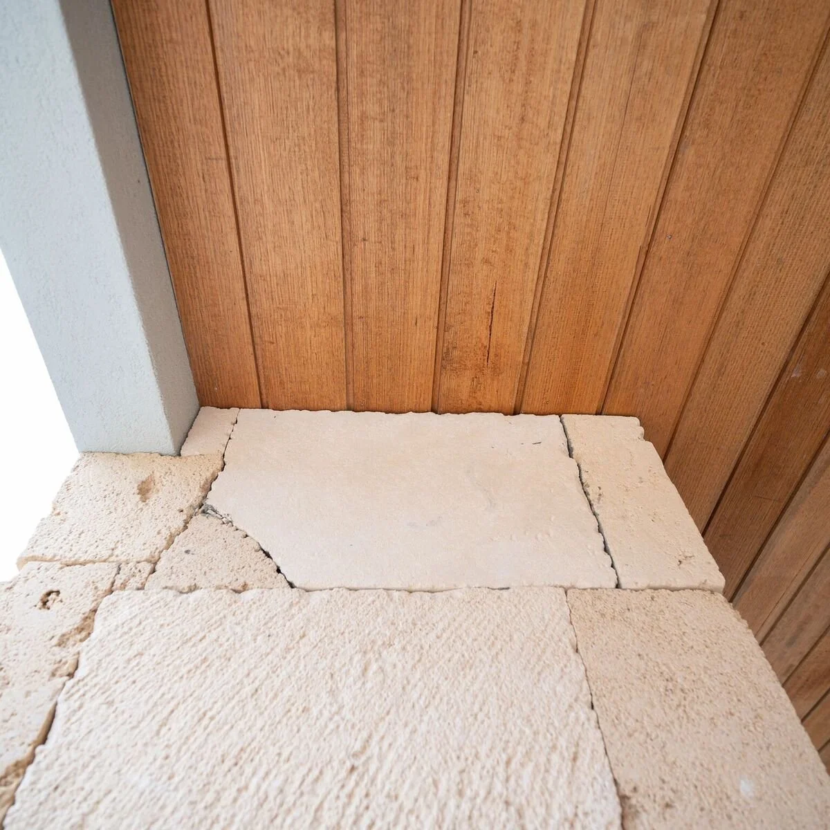 Close-up of a corner where a brick or stone wall meets a wooden paneled wall, showing uneven surfaces and minor cracks.