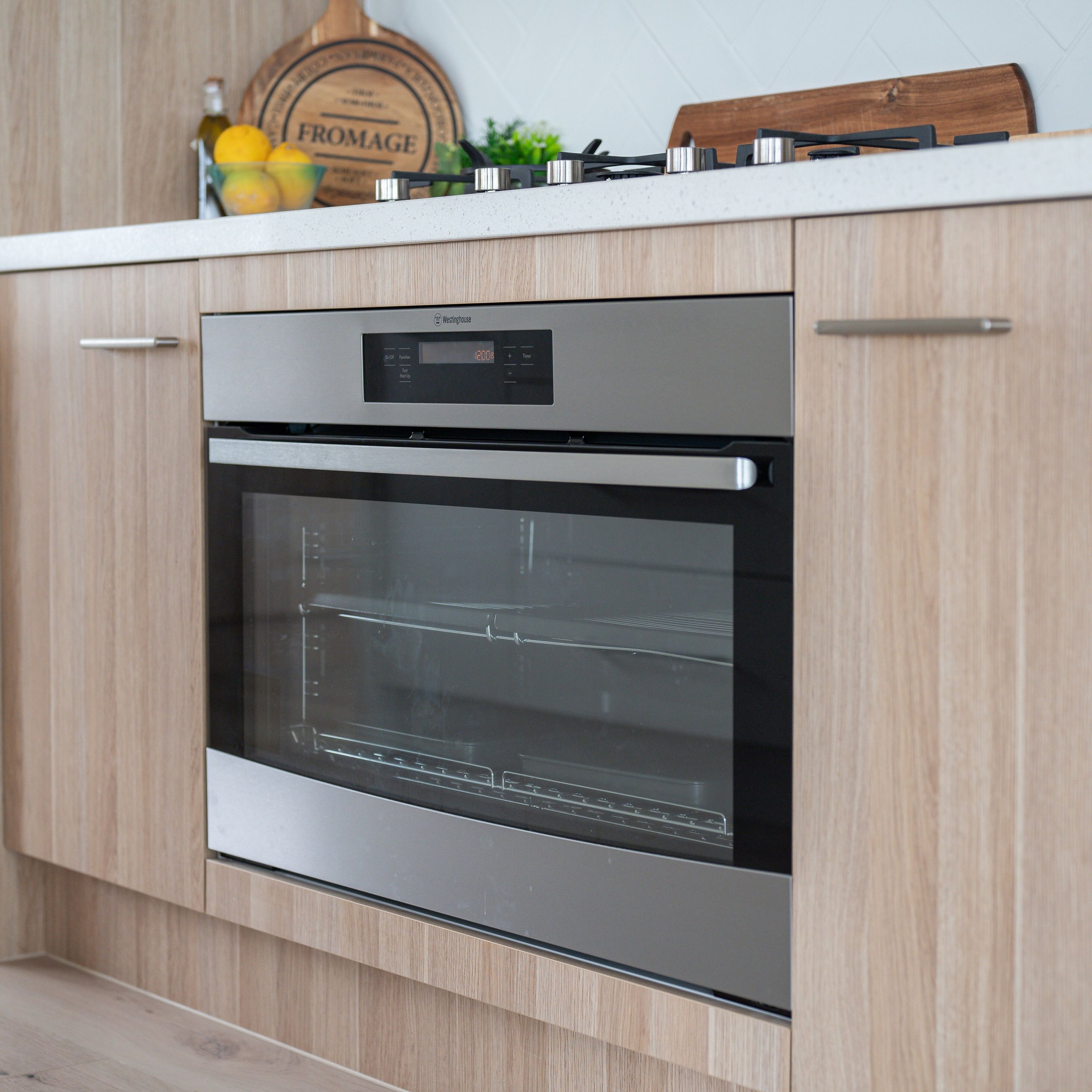Built-in stainless steel oven installed in light wood kitchen cabinet with black control panel and glass door.