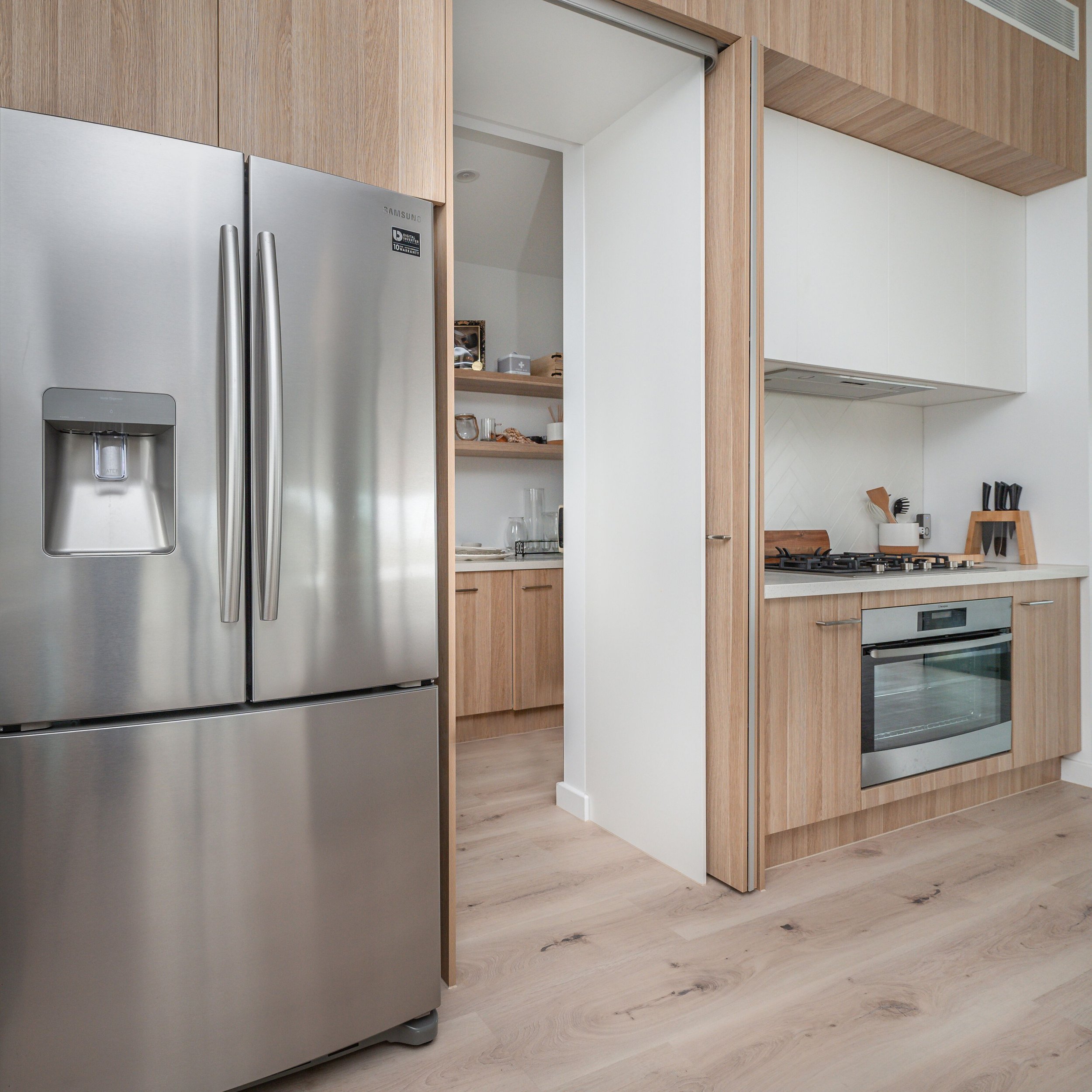 Modern kitchen with stainless steel refrigerator, wooden cabinets, and white countertops.