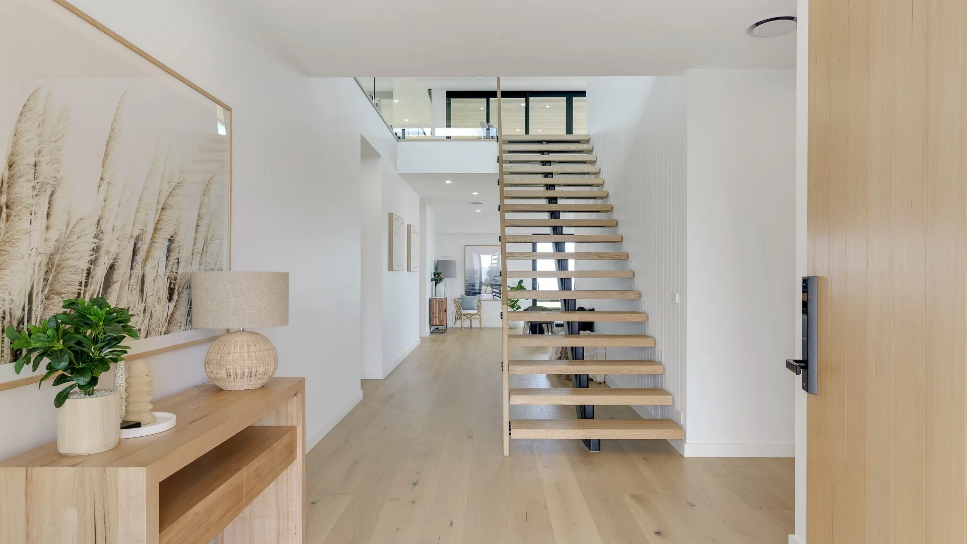 Interior view of a modern home with a wooden staircase, minimalistic decor, white walls, and light wood flooring.