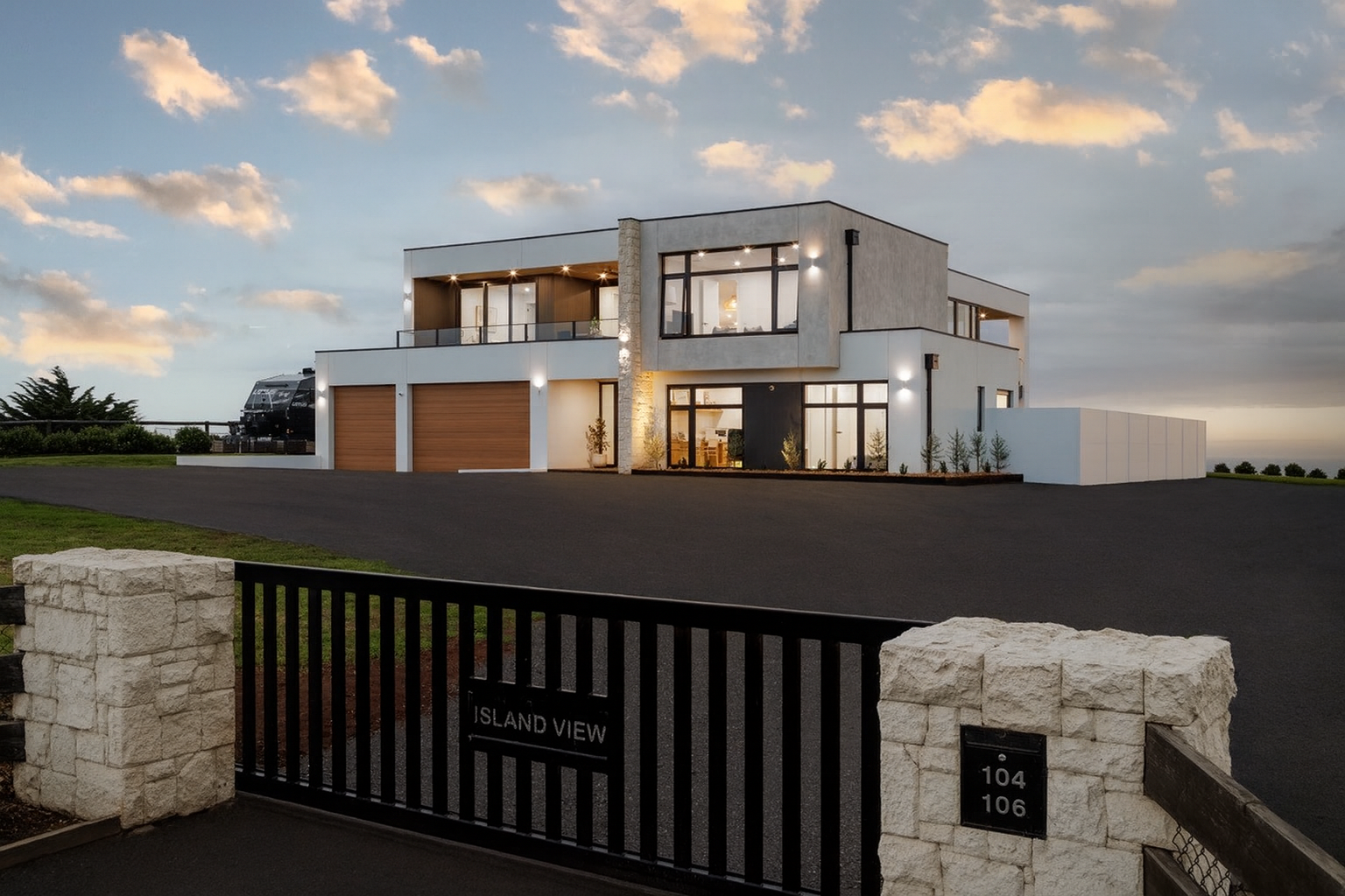 Modern two-story house with three parking spaces and large windows, illuminated at dusk.