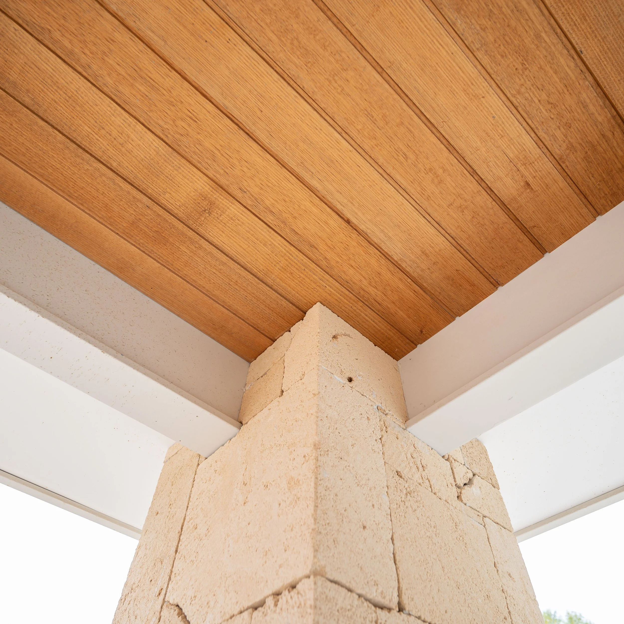 Photo of a corner of a building showing a brick pillar, wooden ceiling, and white support beams.