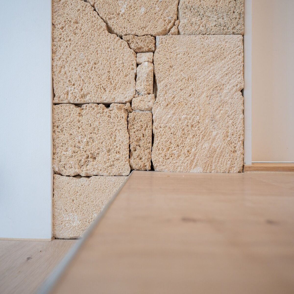 Close-up of a corner wall with large, rough-textured beige stone blocks, white plaster, and a wooden floor.