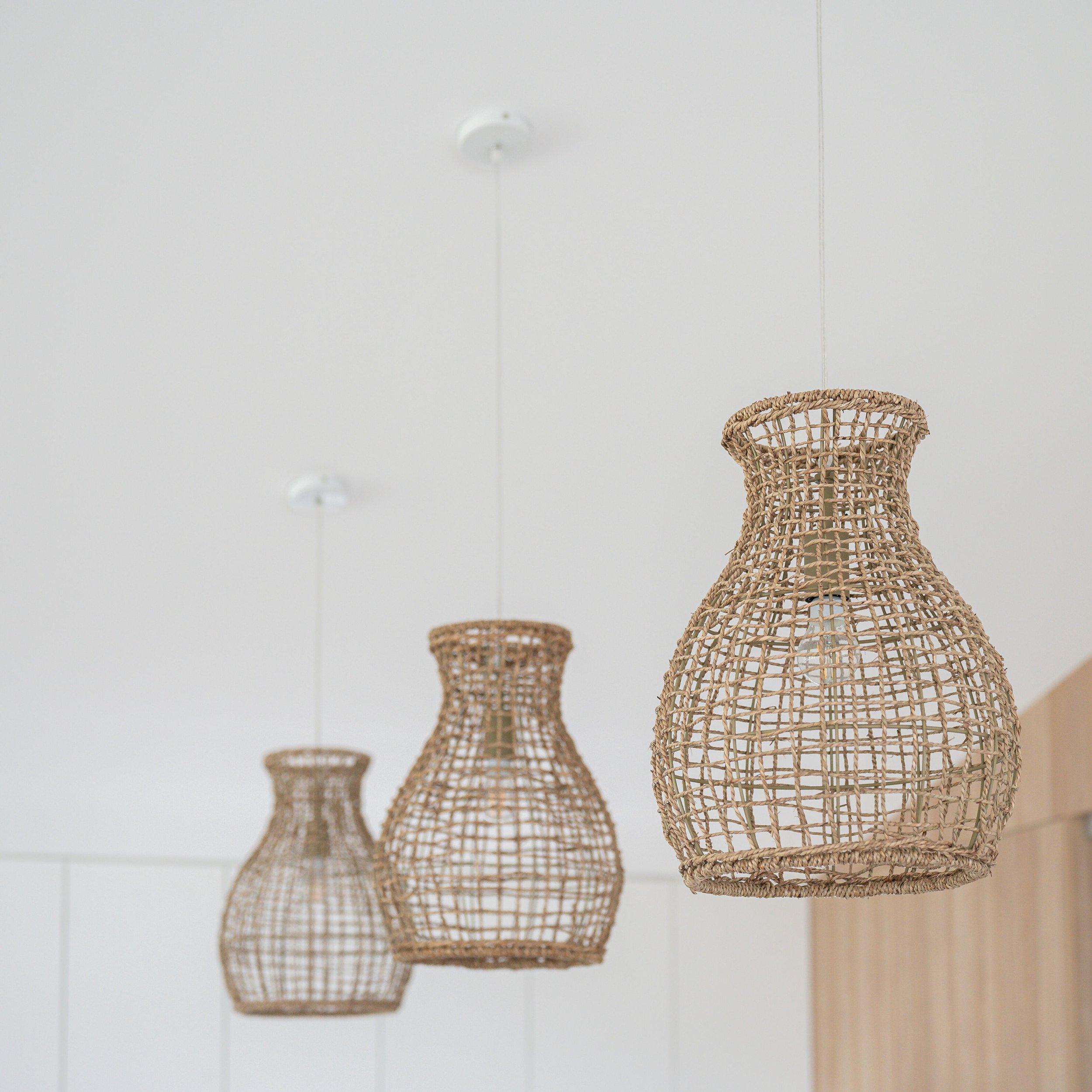 Three wicker pendant light fixtures hanging from the ceiling in a room with white walls.