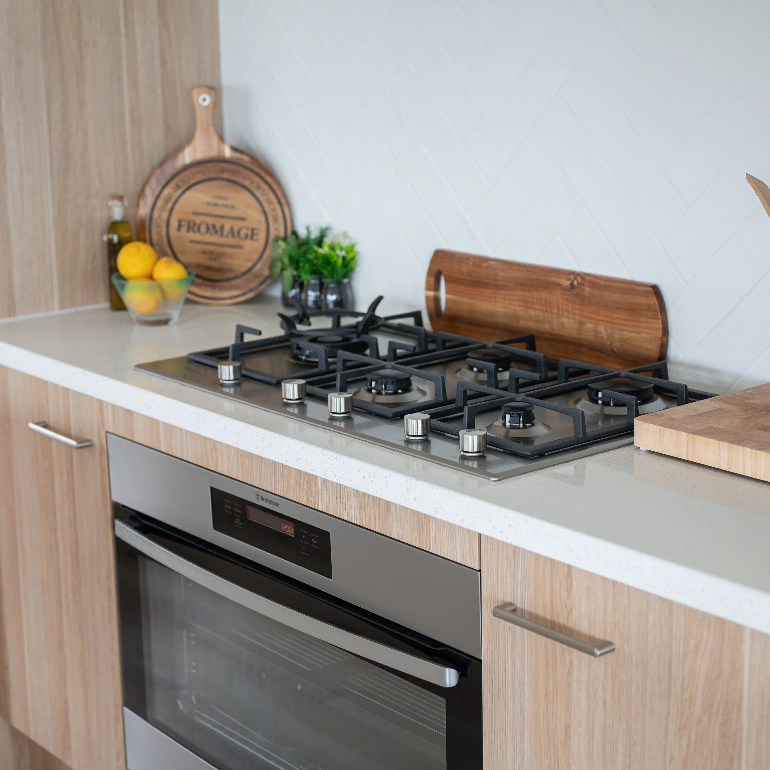 A modern kitchen with a gas stove, wooden cutting board, and decorative items like lemons, herbs, and a cheese platter.
