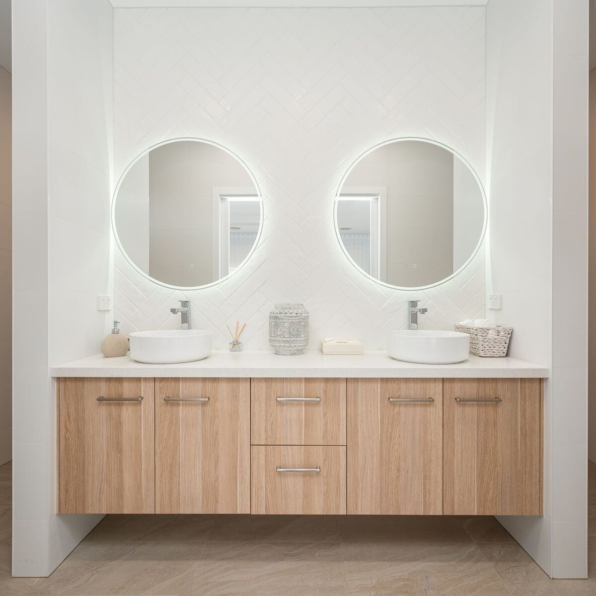Bathroom vanity with two round mirrors, dual sinks, light wood cabinet, and decorative items on the white countertop.