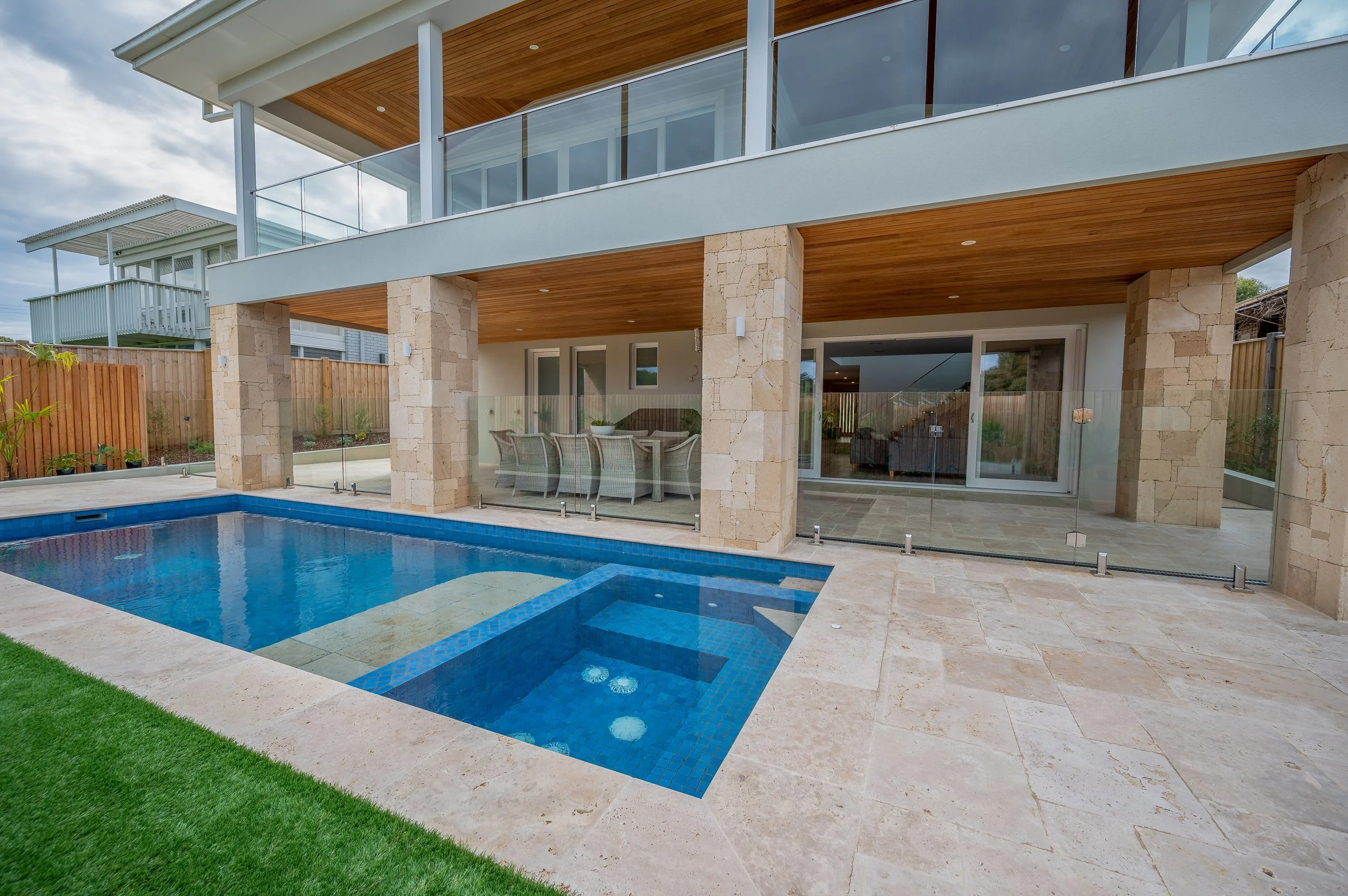 Modern two-story house with an outdoor swimming pool, enclosed by glass fencing and surrounded by a manicured lawn.