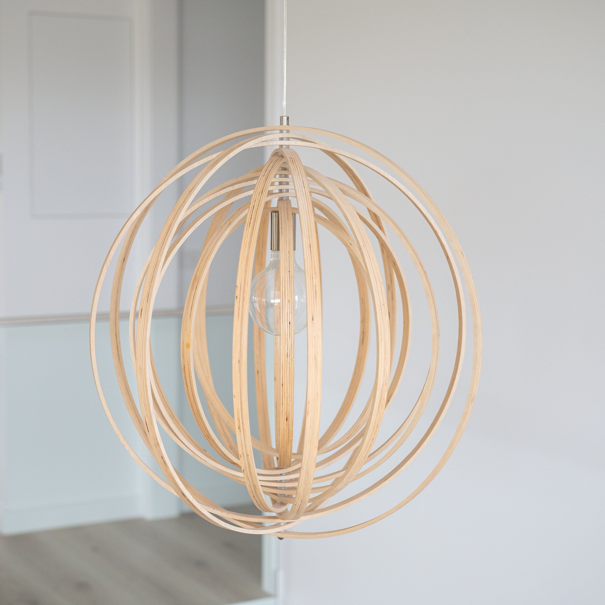 A modern pendant light fixture with wooden slats arranged in an open spherical shape, hanging from a ceiling.