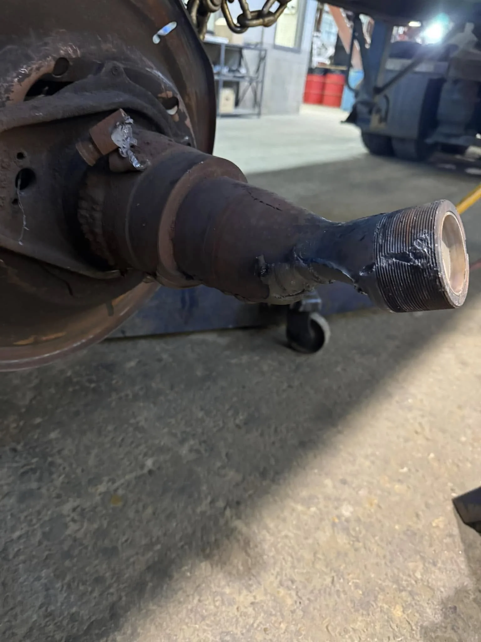 Close-up of a rusty vehicle axle with a new wheel hub installed, in a garage or workshop setting.