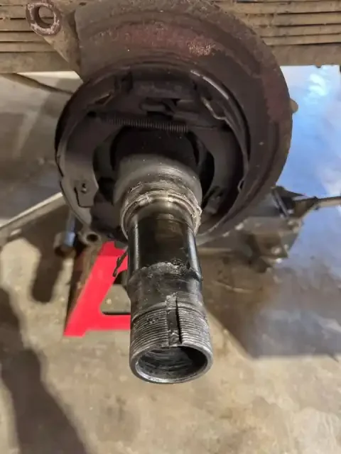 Close-up of a rusted wheel hub and axle on a vehicle, with the axle partially removed, exposing the internal threading.