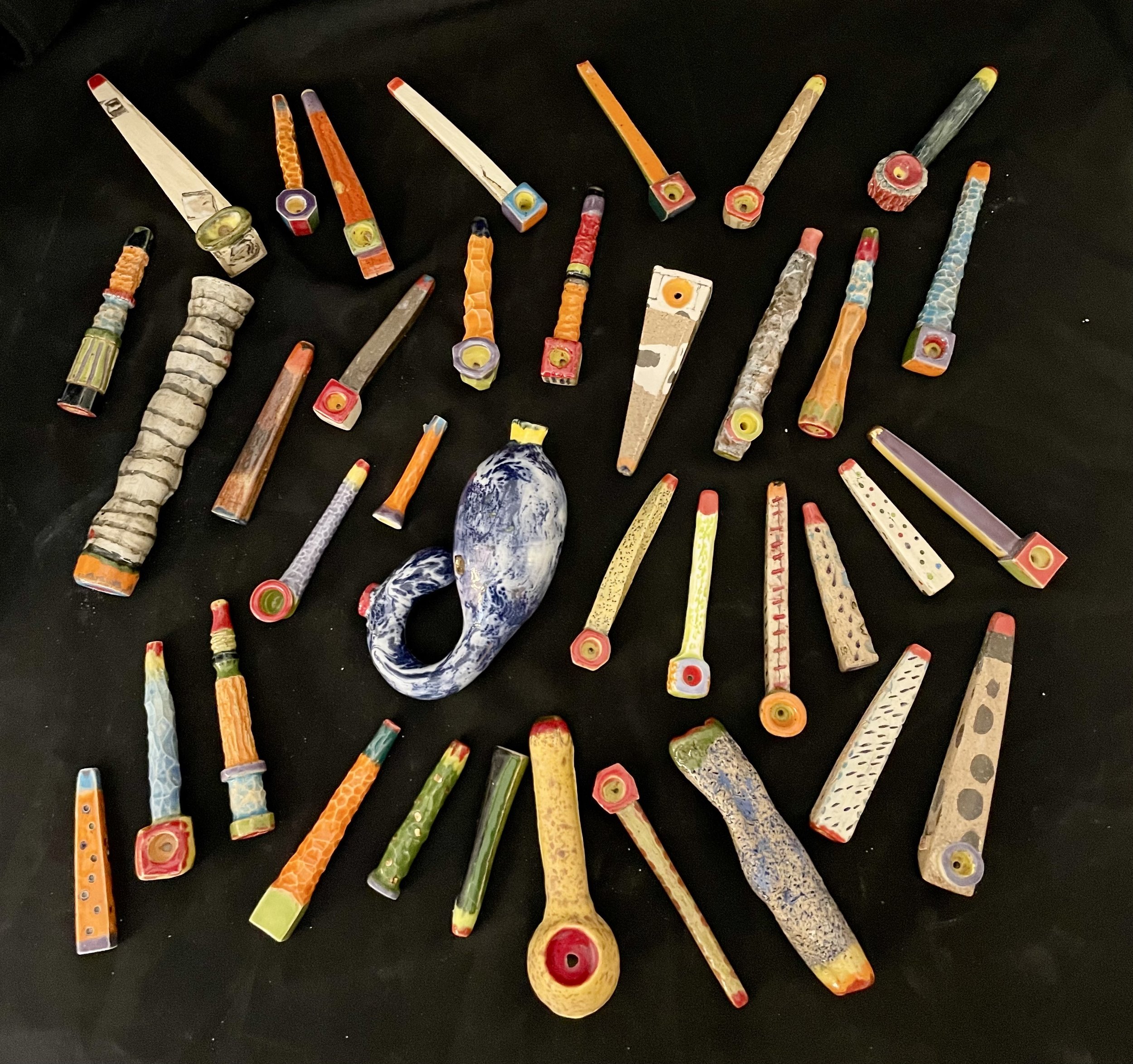 A collection of colorful, handcrafted glass smoking pipes arranged on a black surface.