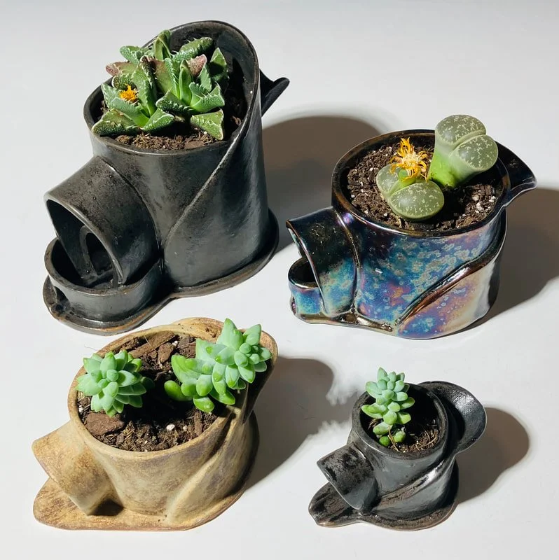 Four ceramic pots shaped like charging stations, each containing different succulent plants, placed on a white surface.