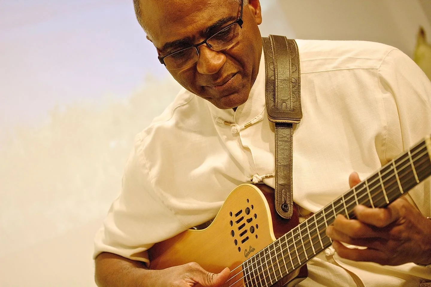 A man wearing glasses and a white shirt playing an acoustic guitar.