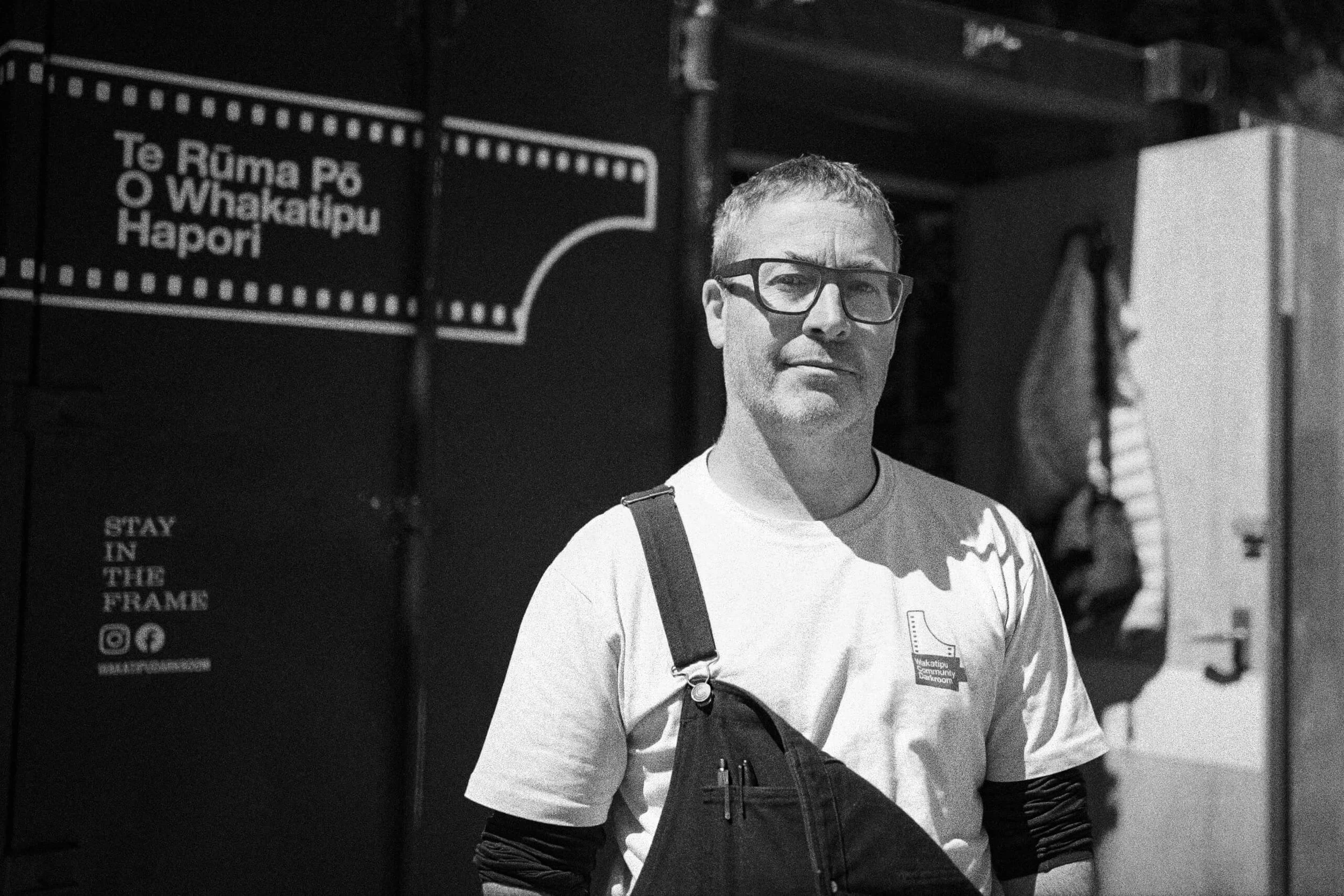 Founder and Guide Paul Green standing outside the Queenstown Darkroom wearing overalls