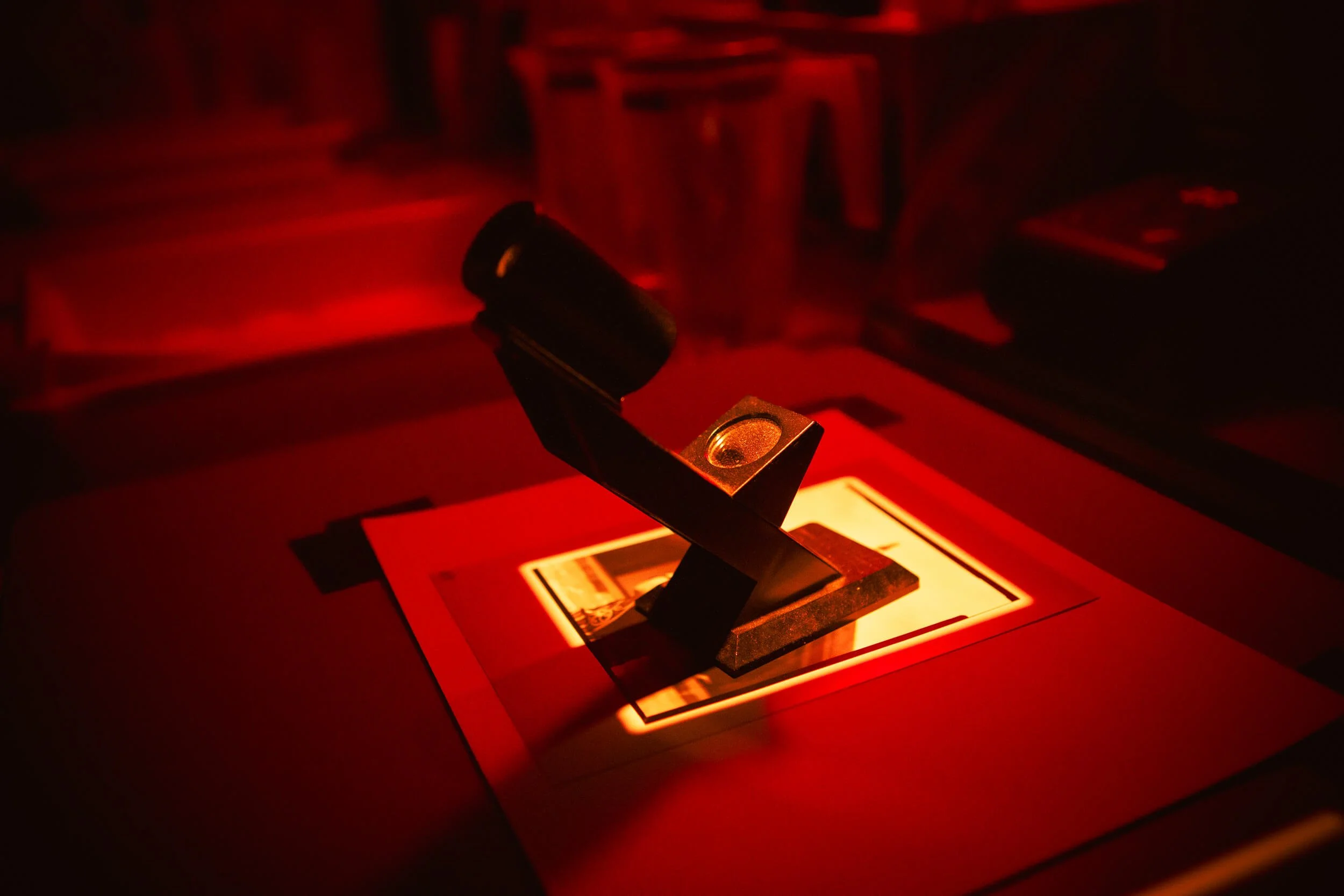 Close-up of a grain focus tool on the enlarger baseboard under the darkroom safe light.