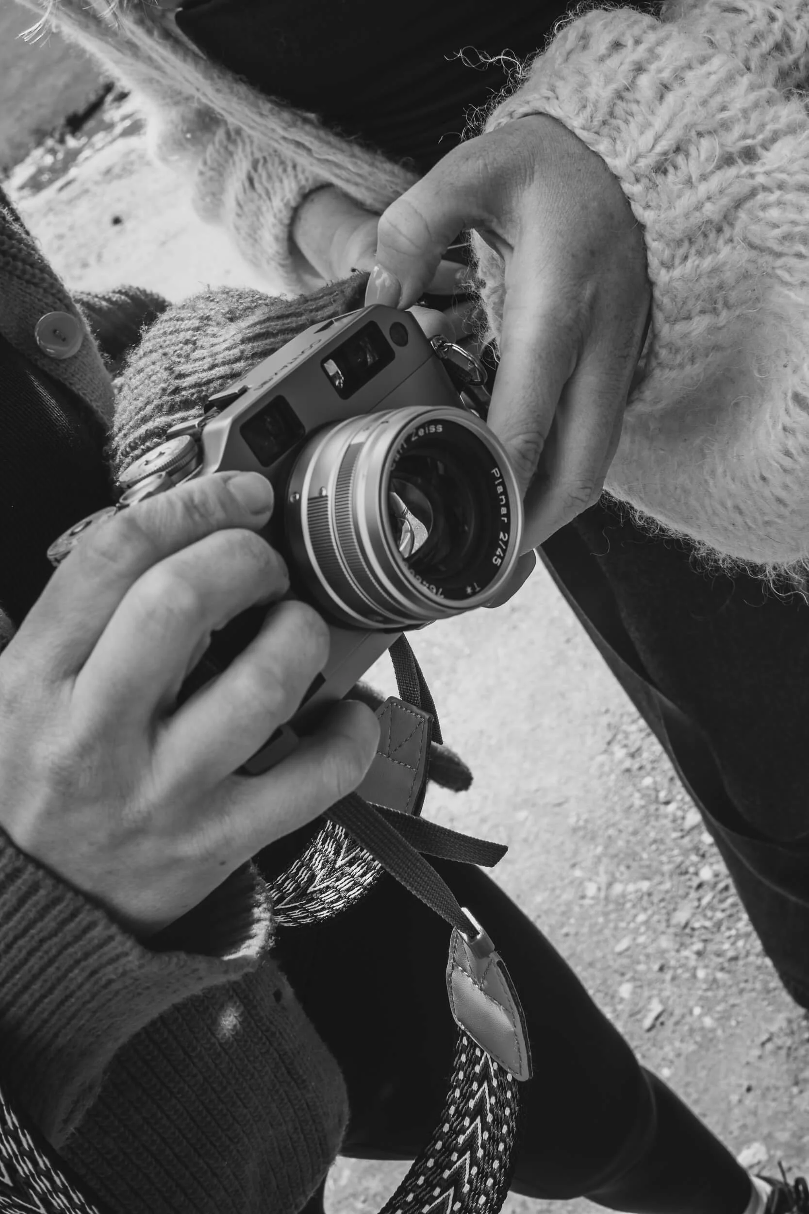 Black and White close-up image of 2 women holding a film camera while another person adjusts it. Photo is taken outdoors somewhere in Queenstown.
