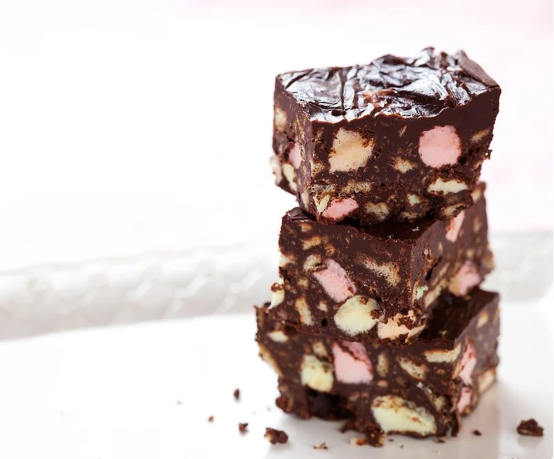 Stack of three slices of Rocky Road with pink and white marshmallows, chocolate chunks, on a white plate.