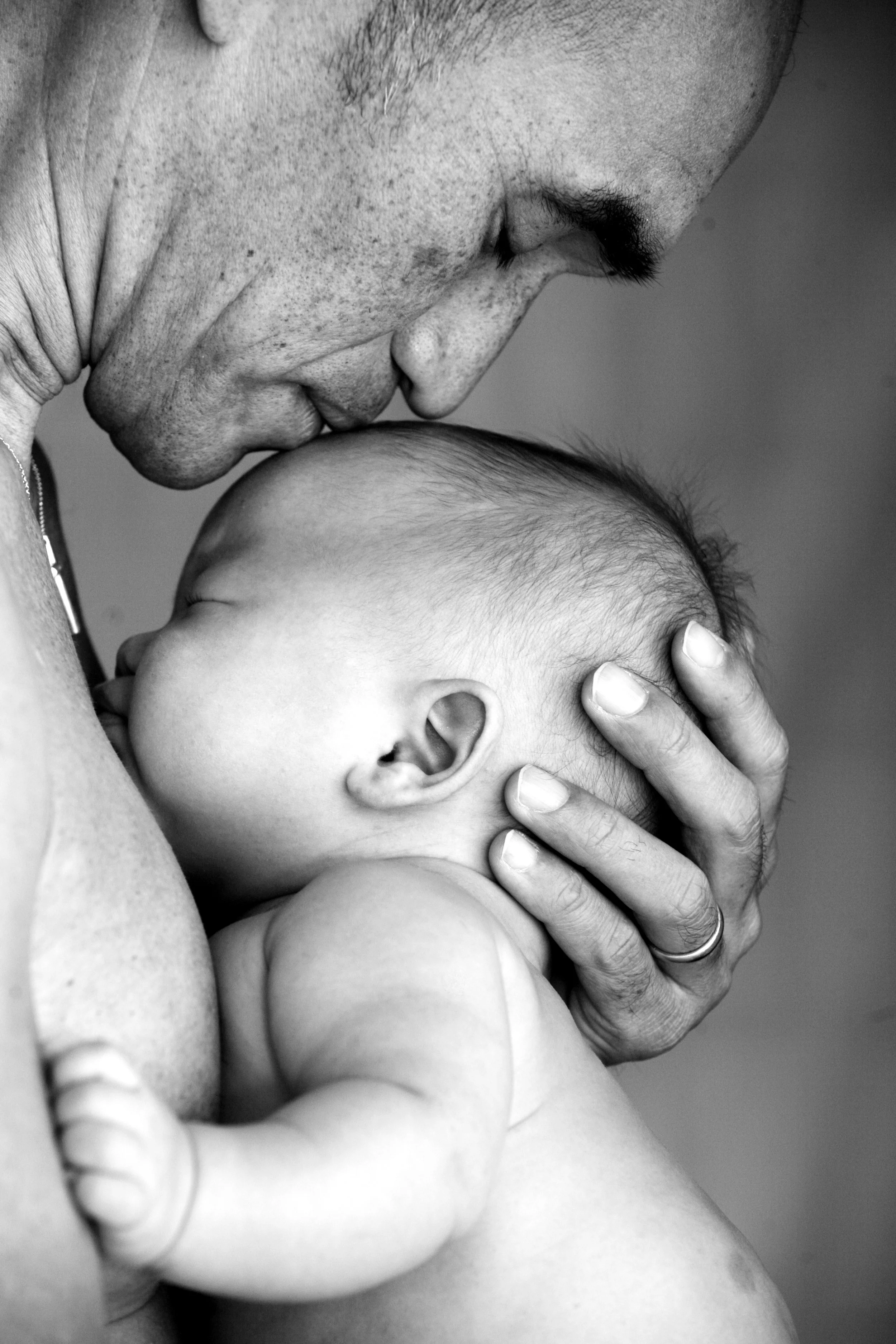 A close-up black and white photograph of an adult man gently holding and kissing a sleeping baby on the forehead.