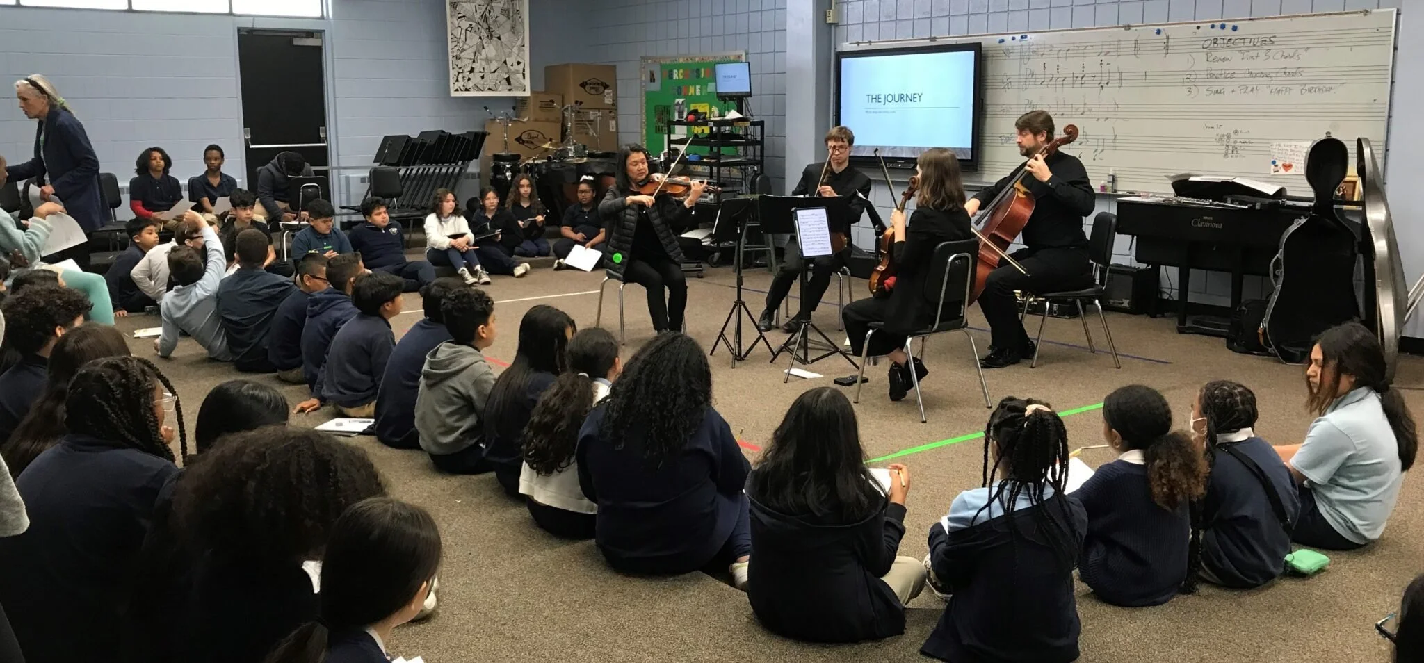 Students sit on the floor around a GBS string quartet during a school visit