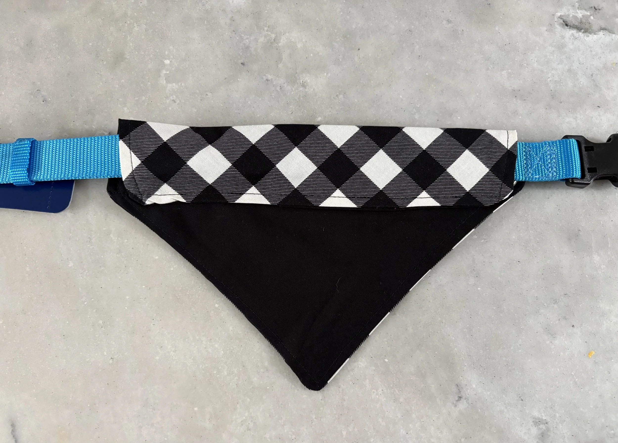 A black bandana with a white checkered pattern attached to a blue strap with a black plastic buckle.