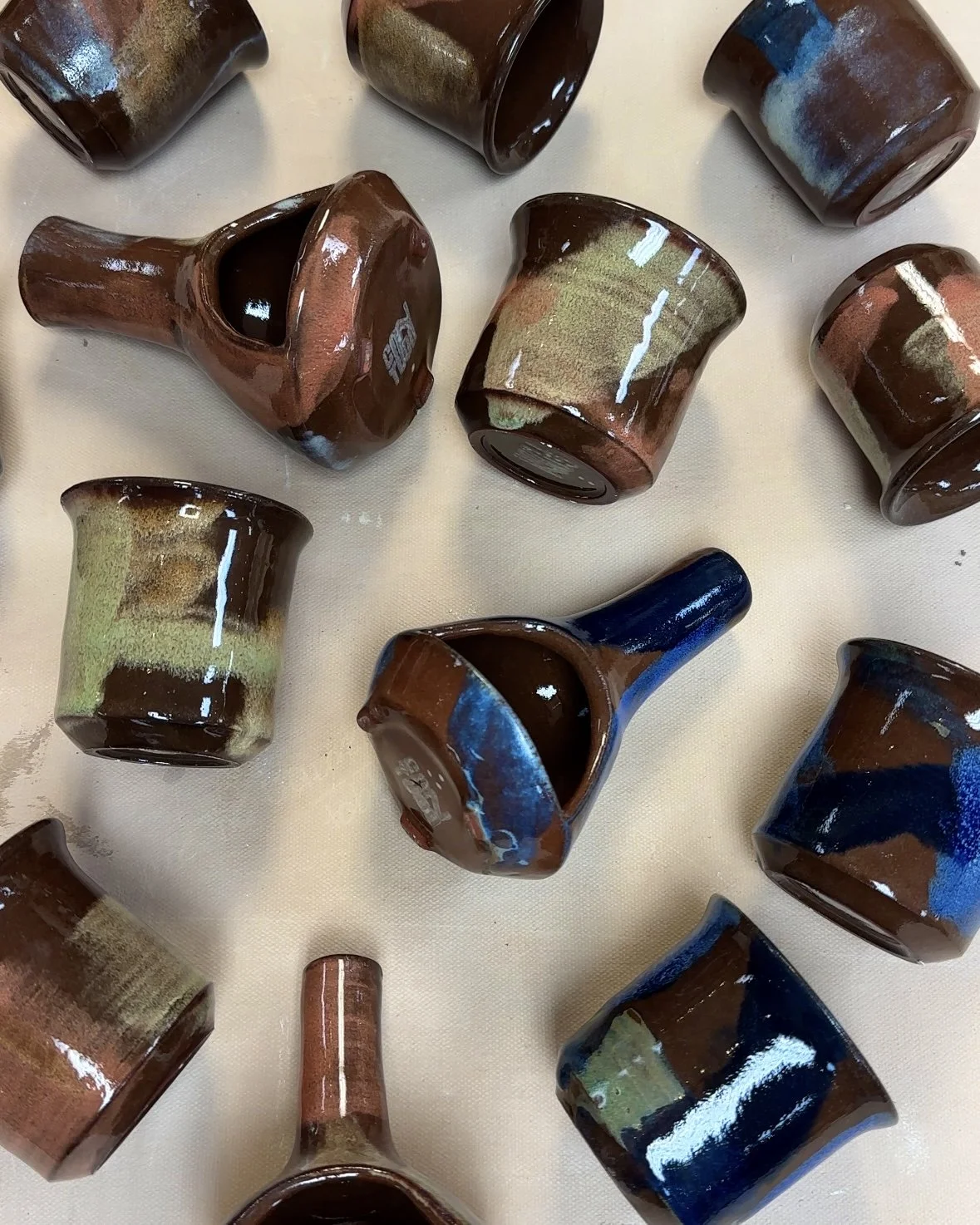 Clay pots and cups arranged on a table, with some upside down and some right side up, in various colors and glaze patterns.