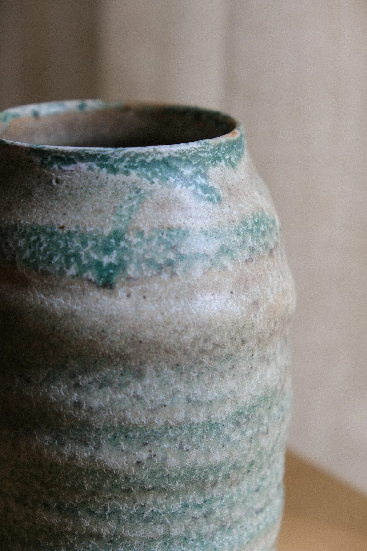 Close-up of a textured ceramic vase with beige and green glaze.