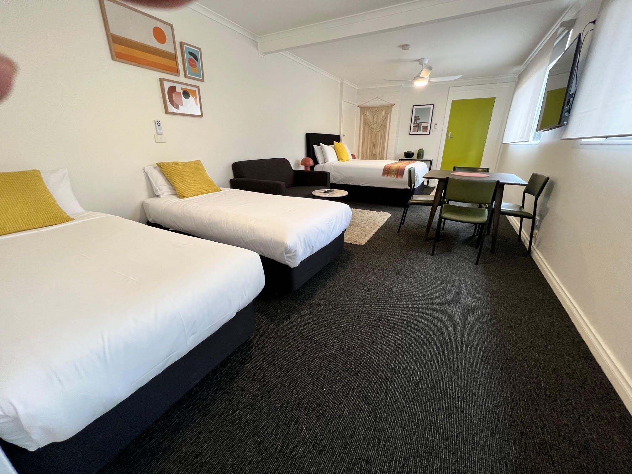 A hotel room with two beds, artwork on the wall, a black sofa, a small table, a dining table with chairs, and a window with white curtains.