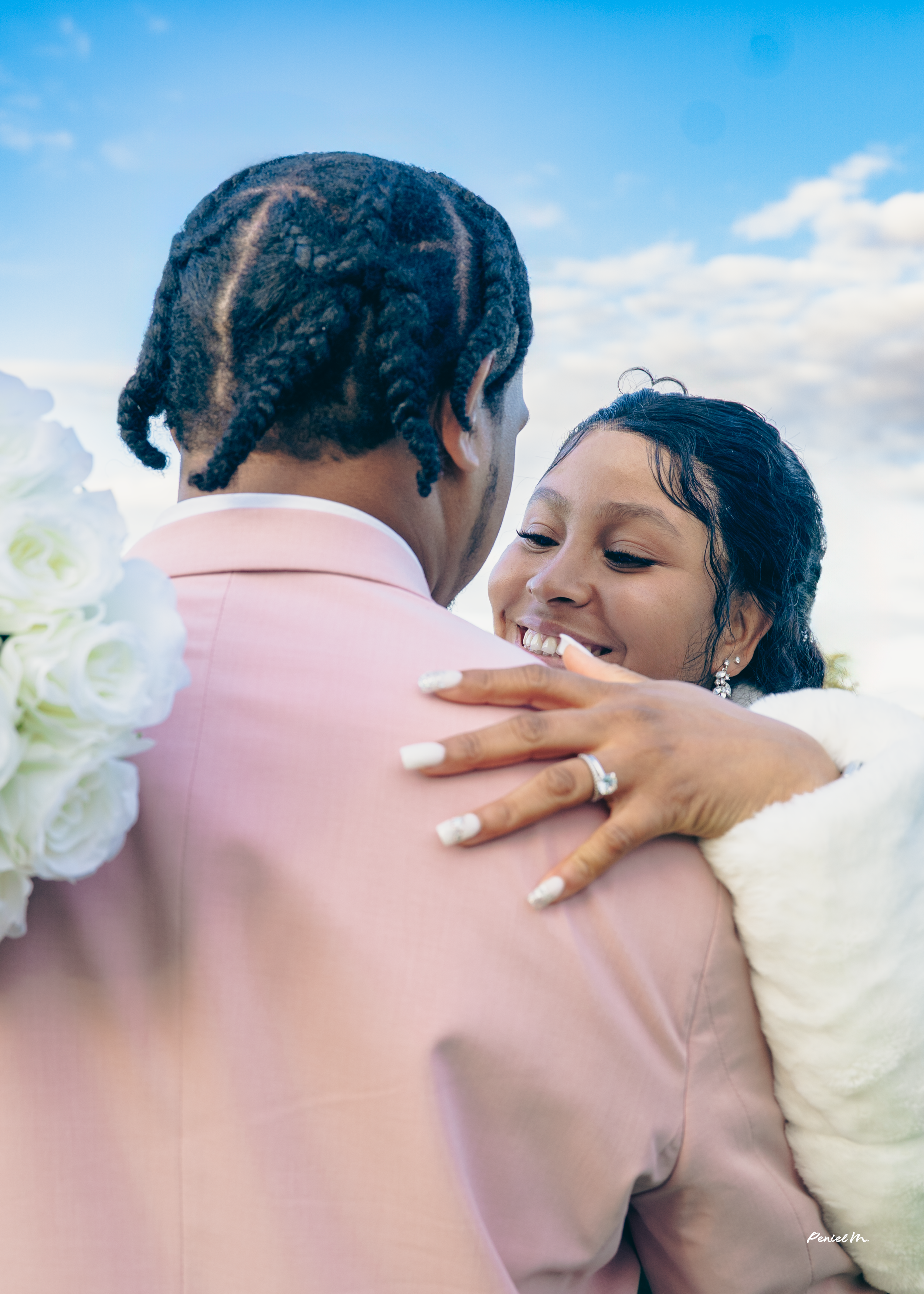 A newlywed couple sharing a dance outdoors, smiling and embracing each other, with the bride showing her wedding ring.
