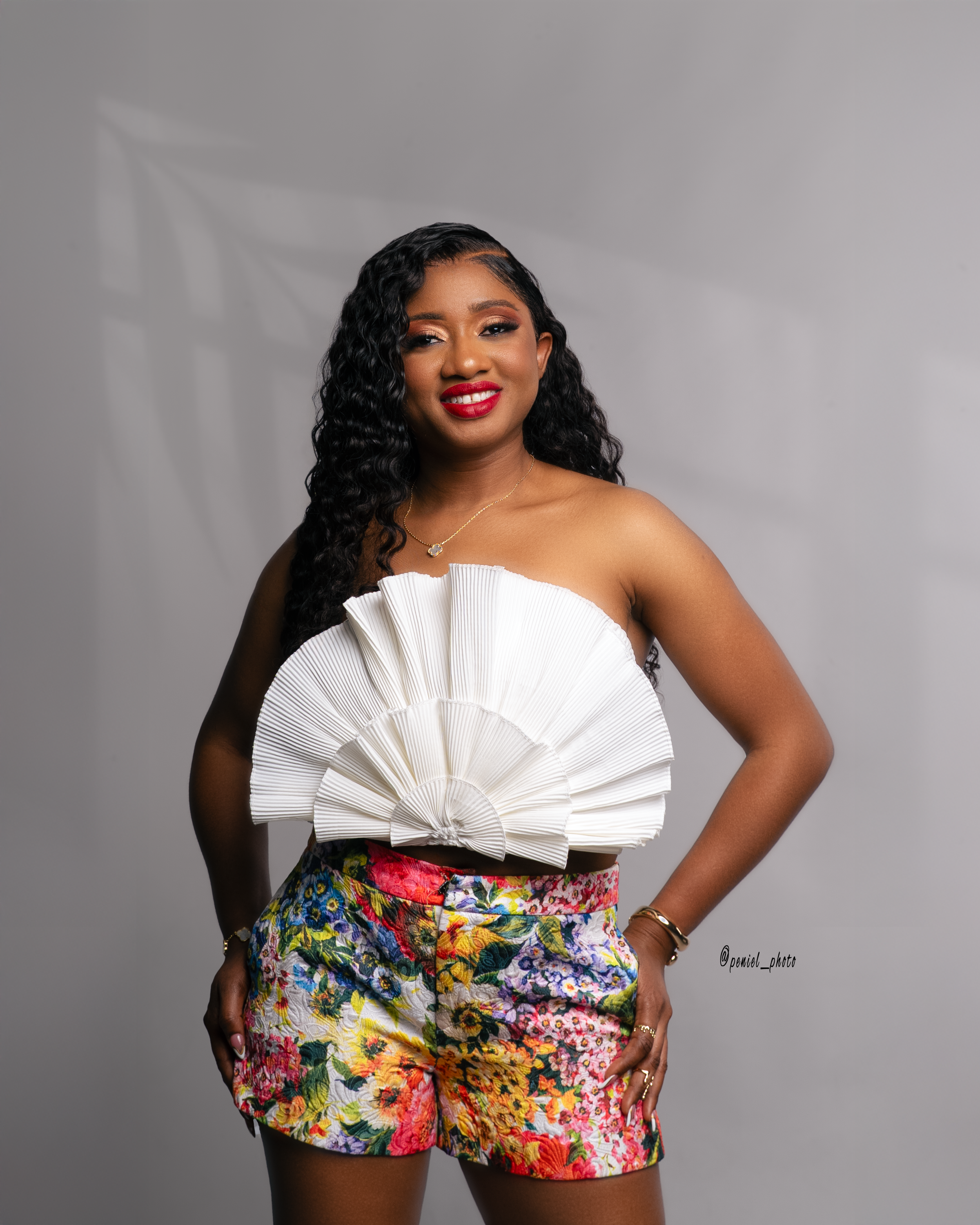 Woman wearing a white ruffled top and floral shorts, posing with a smile against a plain background.
