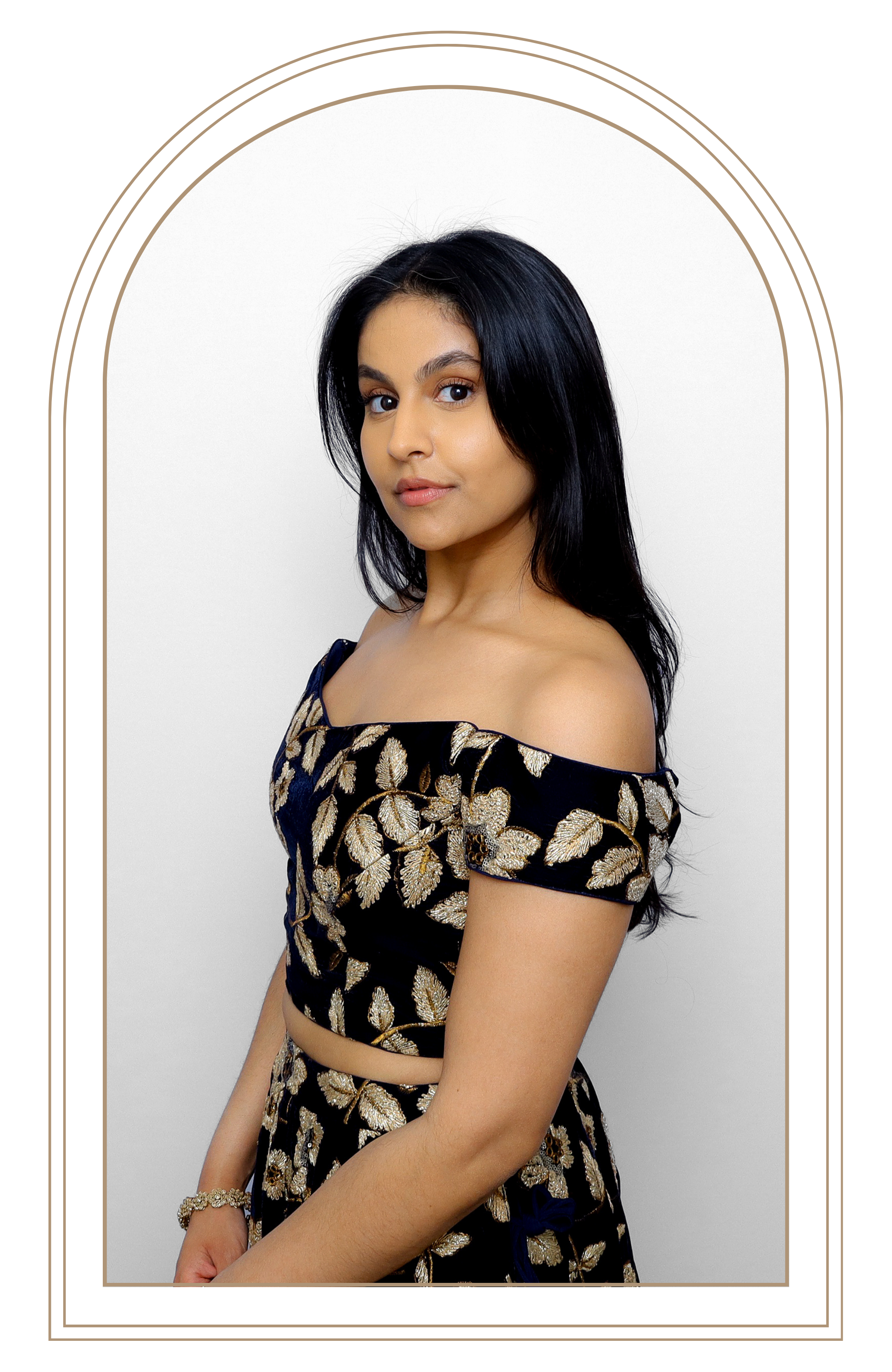 Portrait of a young woman with long black hair, wearing an off-the-shoulder black dress with gold leaf pattern, standing in front of a plain white background.