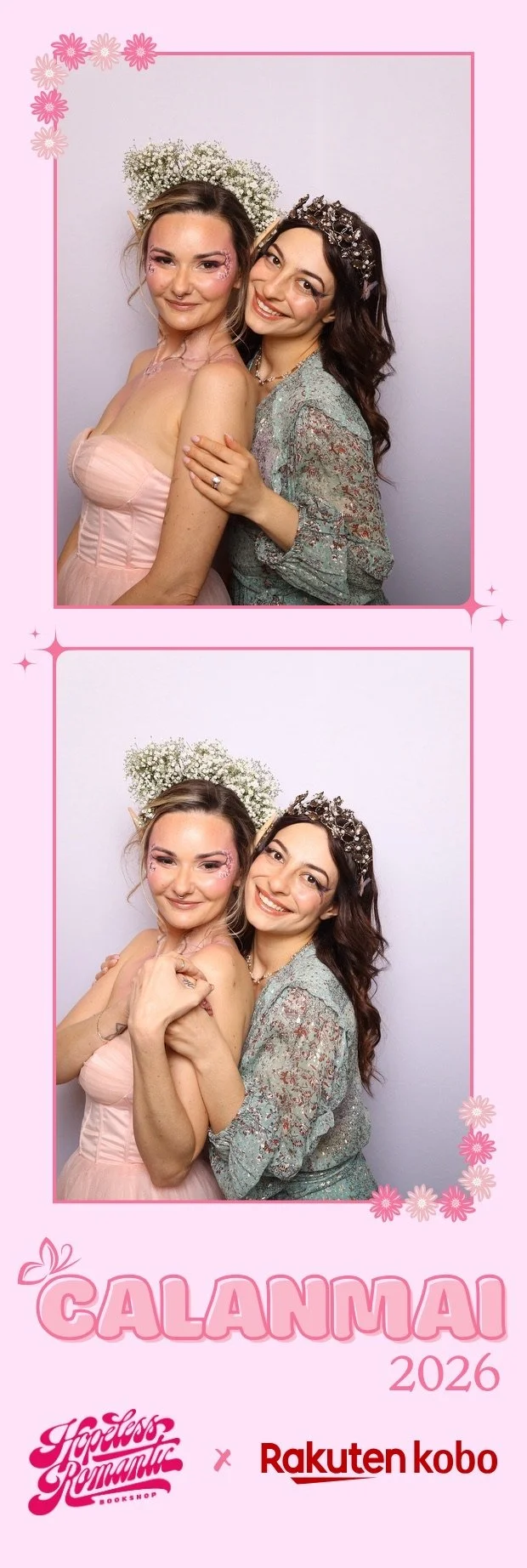 Two women dressed in fantasy-inspired costumes, one with fairy wings and pink makeup, and the other with a floral headband and crown, posing together in a photo booth with a pink background decorated with flowers, at an event called 'Calanmai 2026'.