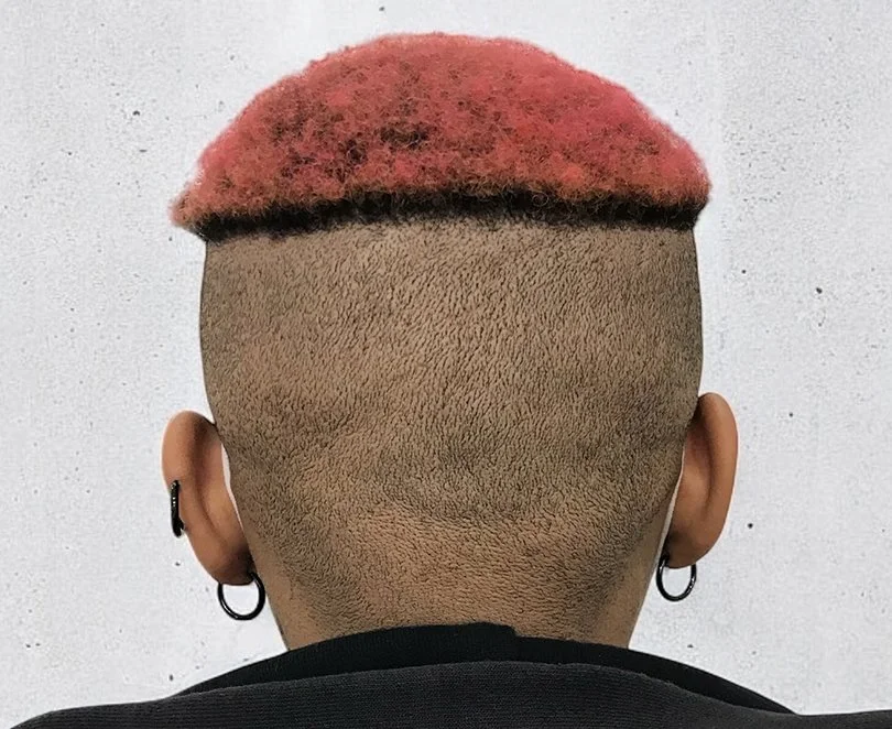 Back of a person's head with a short faded haircut and pink dyed hair on top, wearing earrings