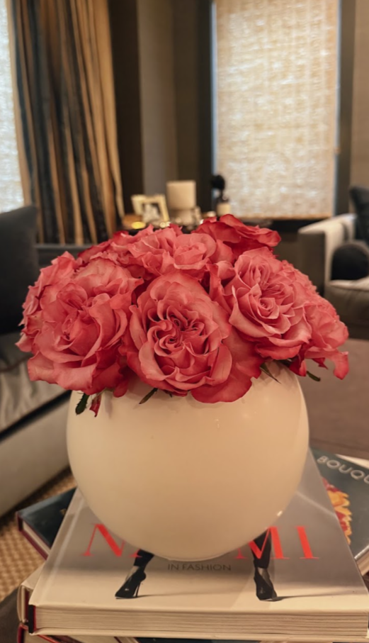 A white round vase filled with pink roses on top of a fashion magazine.