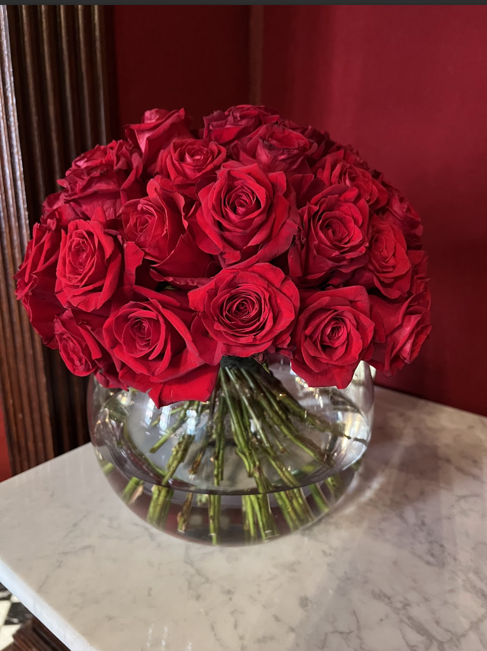 A large bouquet of red roses in a clear glass vase placed on a white marble surface.