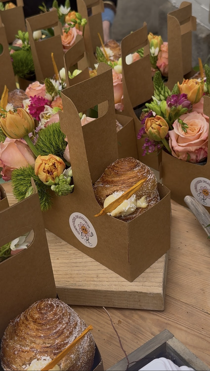 Boxed bakery items with flowers surrounding them on a wooden table.